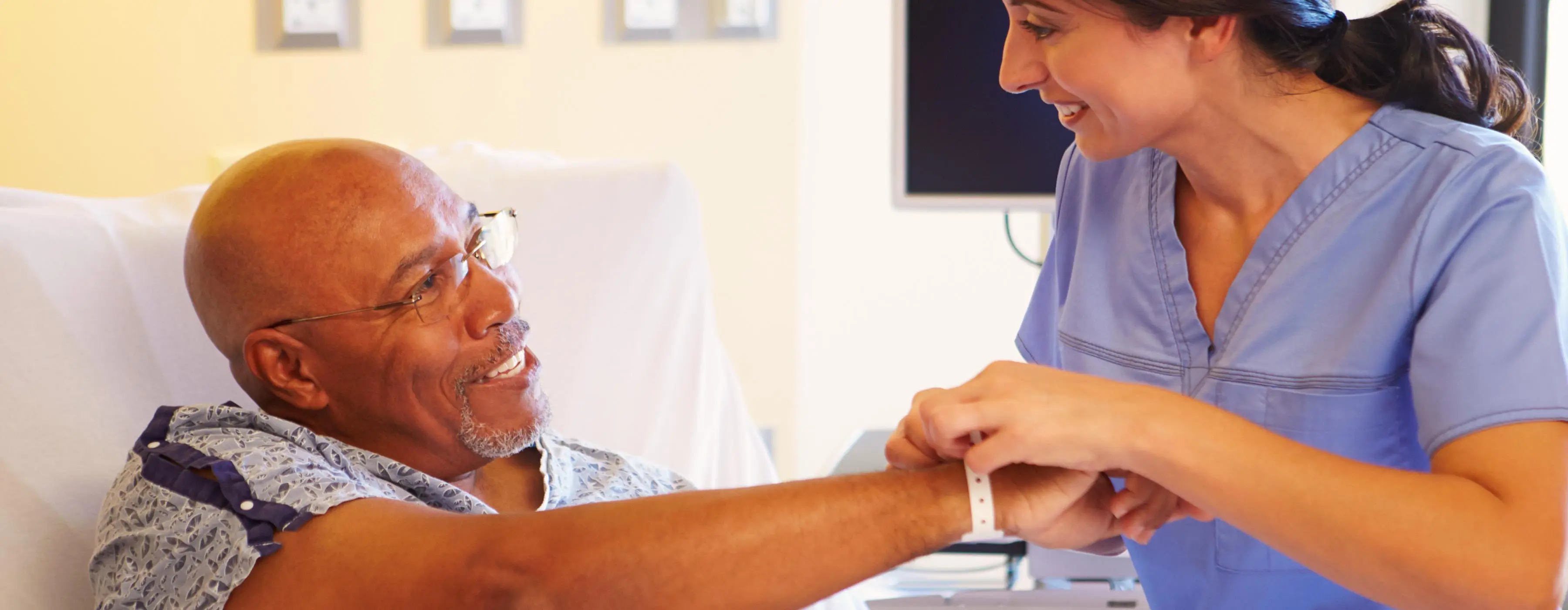 Foto de uma profissional de saúde em ambiente hospitalar, prestando atendimento a um homem idoso.