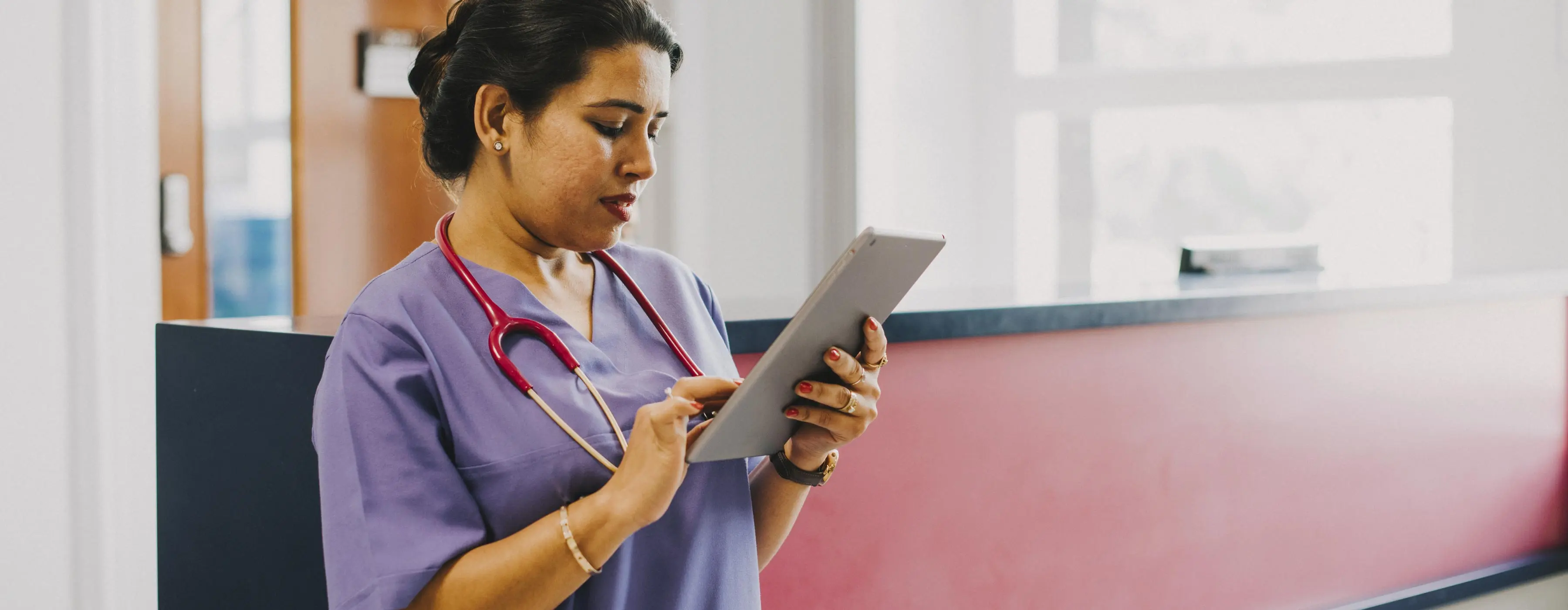 Foto de uma mulher profissional de saúde em ambiente hospitalar mexendo em tablet.