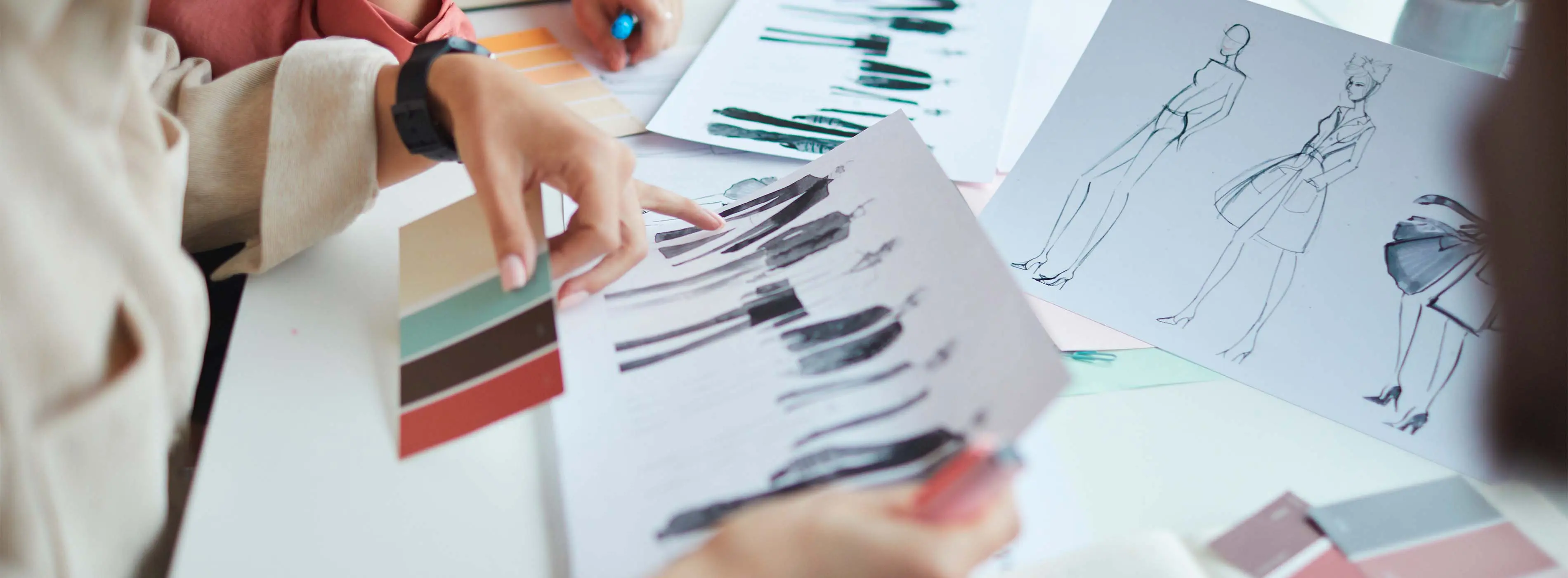 Foto em close de croquis de manequim de roupas sendo analisado por uma pessoa que verifica também amostras de cores.