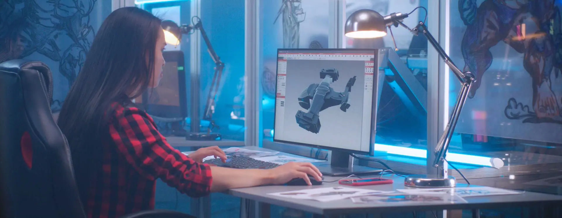 Foto de jovem mulher de cabelos longos e camisa xadrez vermelha e preto em frente ao computador manuseando software de animação em 3D