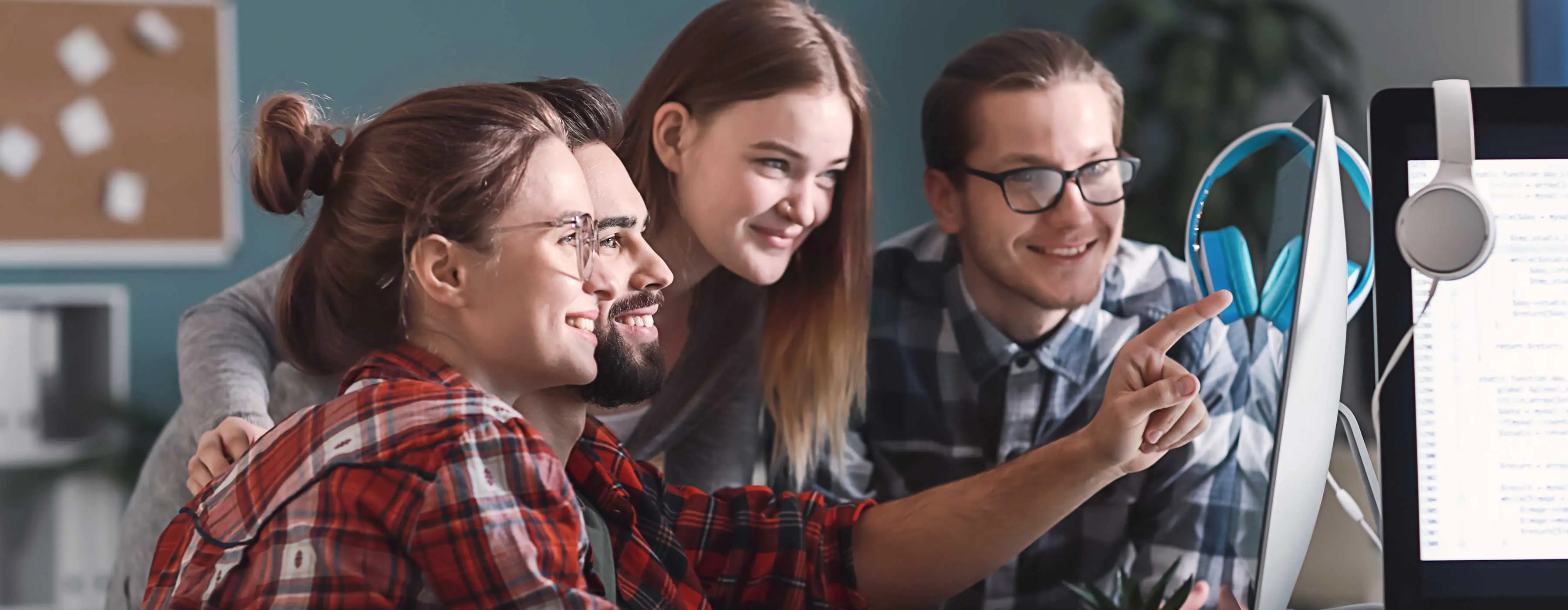 Equipe de programadores observando dado em monitor de MAC em escritório.