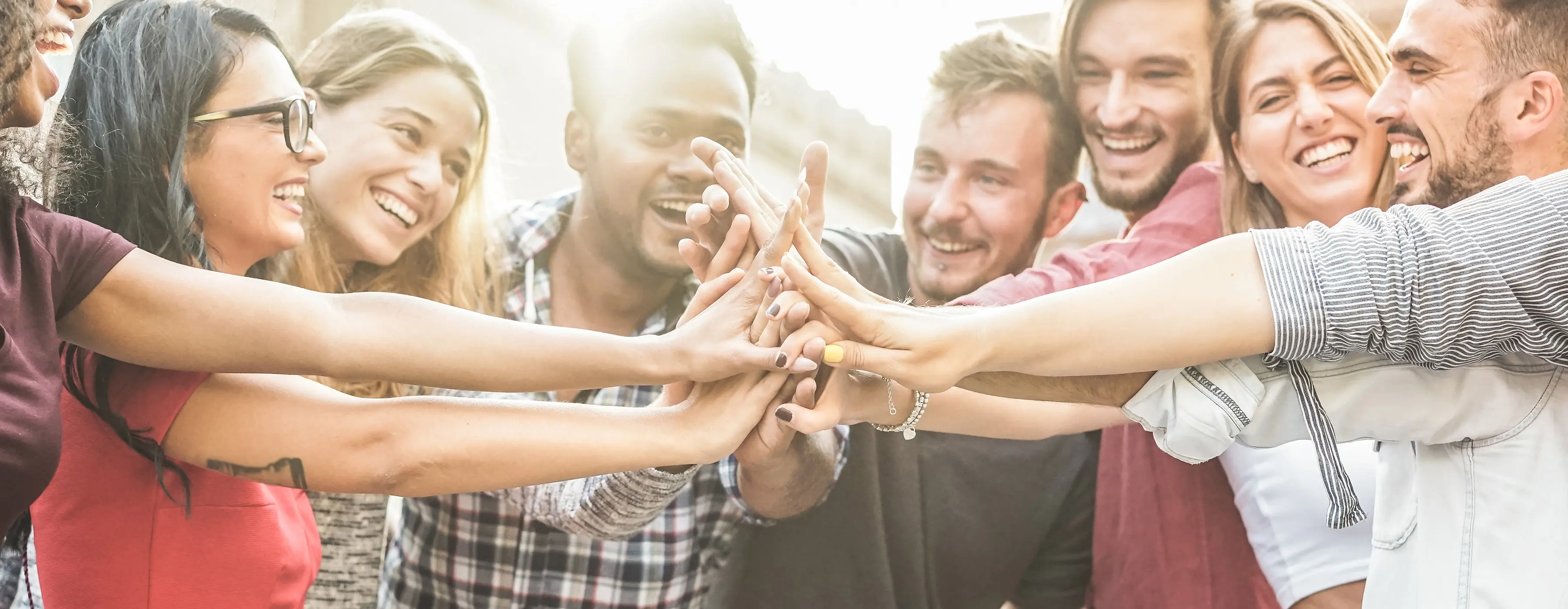 Foto de um grupo com 9 pessoas sorrindo e com as mão levadas ao centro da roda