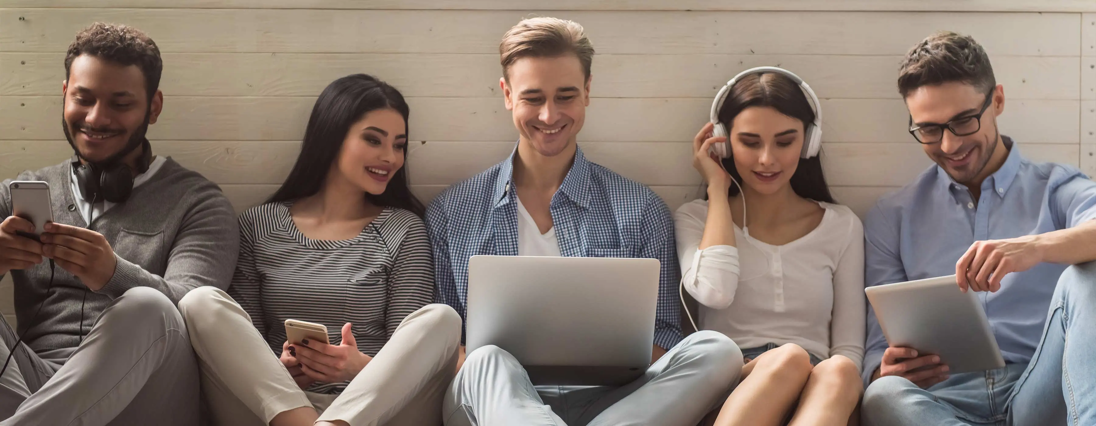 Foto de grupo de pessoas sentadas, sorrindo e olhando os dispositivos móveis que seguram.