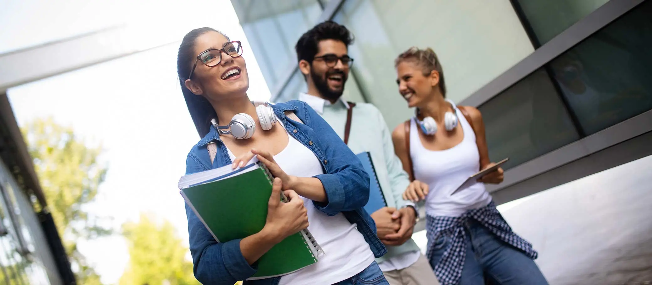 Imagem de pessoas sorrindo e carregando materiais de estudo, como caderno e tablet.
