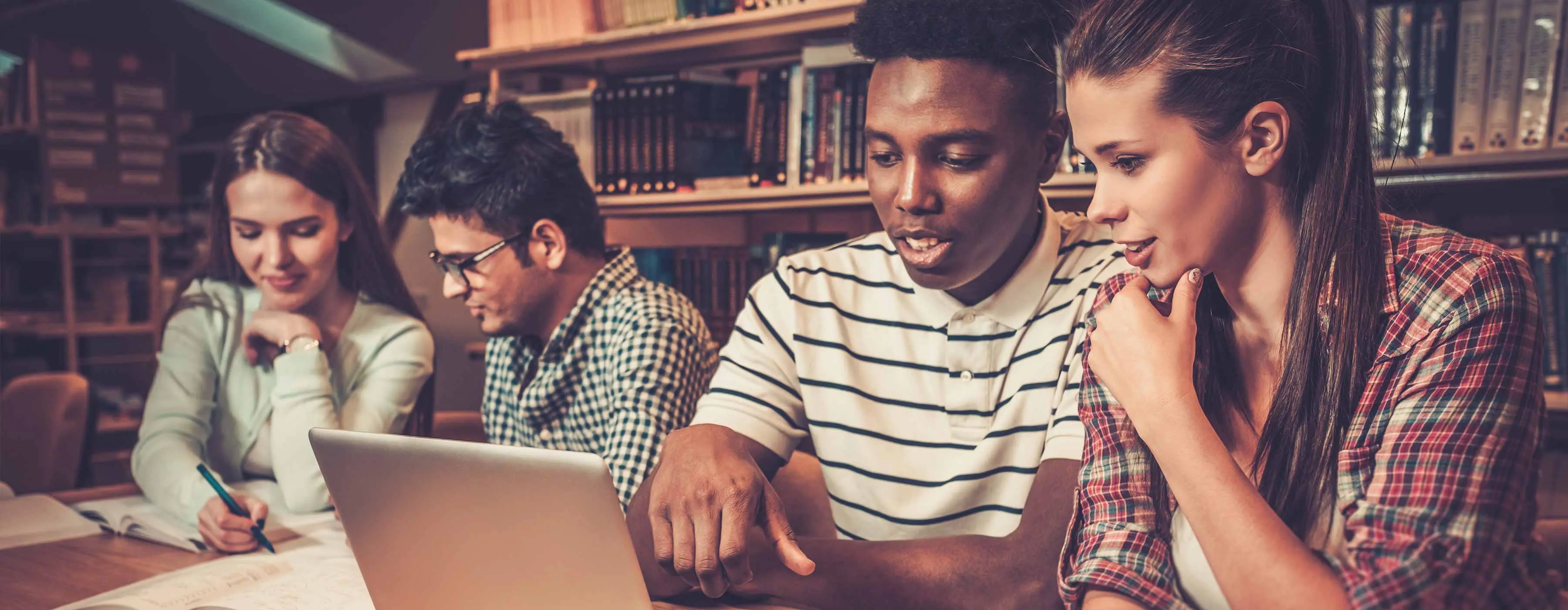 Foto de um grupo de pessoas em uma biblioteca estudando com livros e um computador