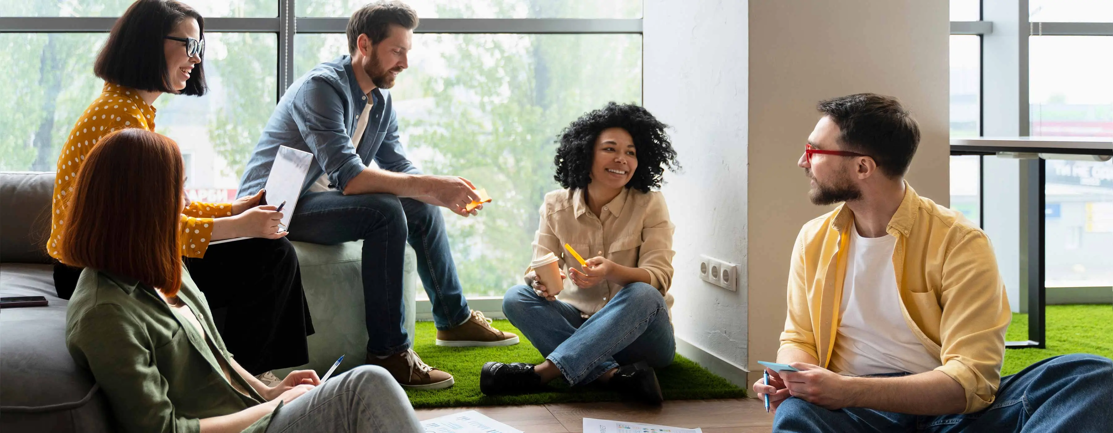 Foto de um grupo de pessoas que está conversando e sentado no chão de uma sala
