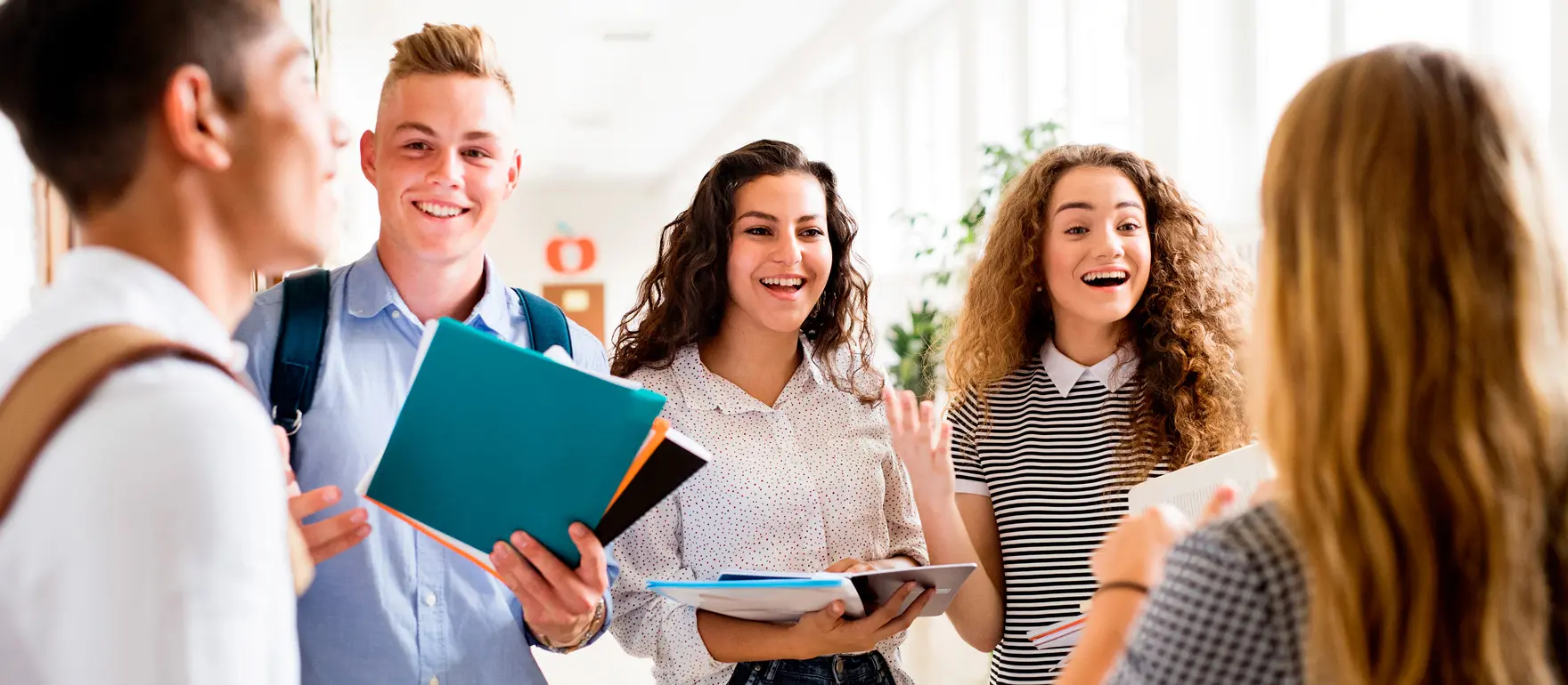 Foto de um grupo de adolescentes conversando enquanto seguram livros e cadernos