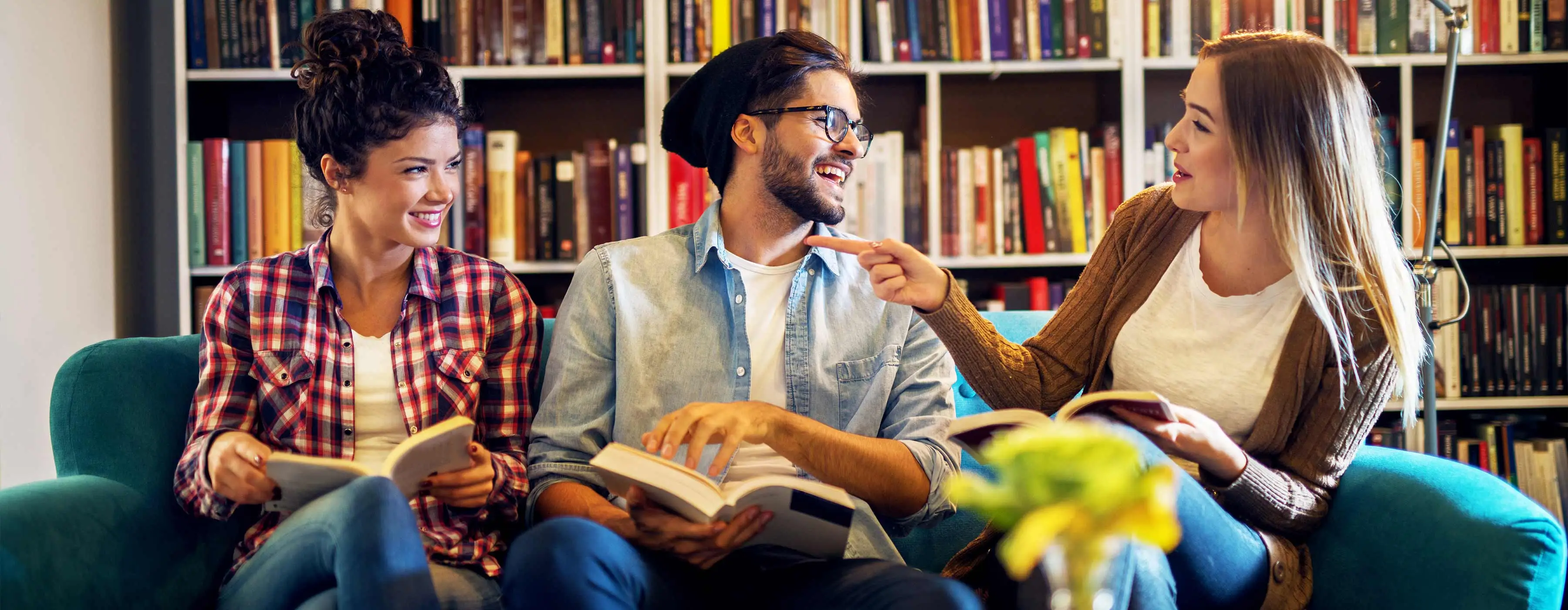 Foto de pessoas conversando e sorrindo, enquanto estão sentadas em um sofá e seguram livros nas mãos.