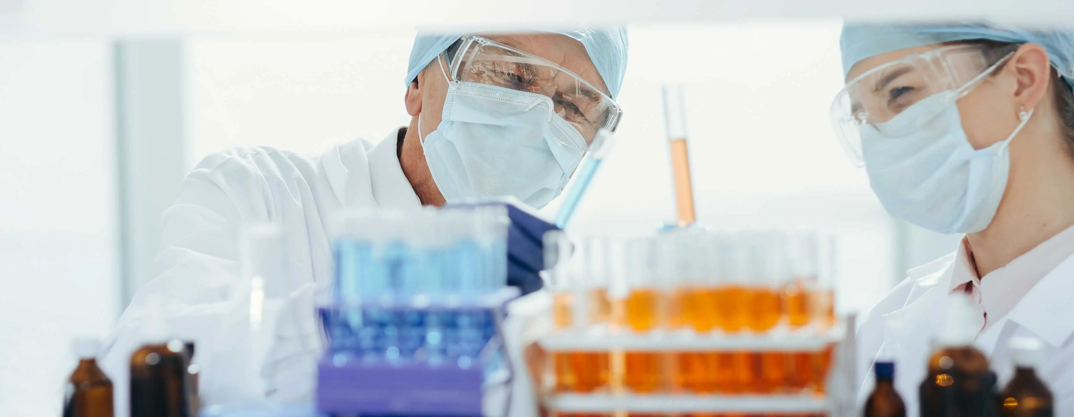 Foto em close de mãos de profissional da saúde com luvas cirúrgicas e avental manuseando tubos de ensaio em laboratório.
