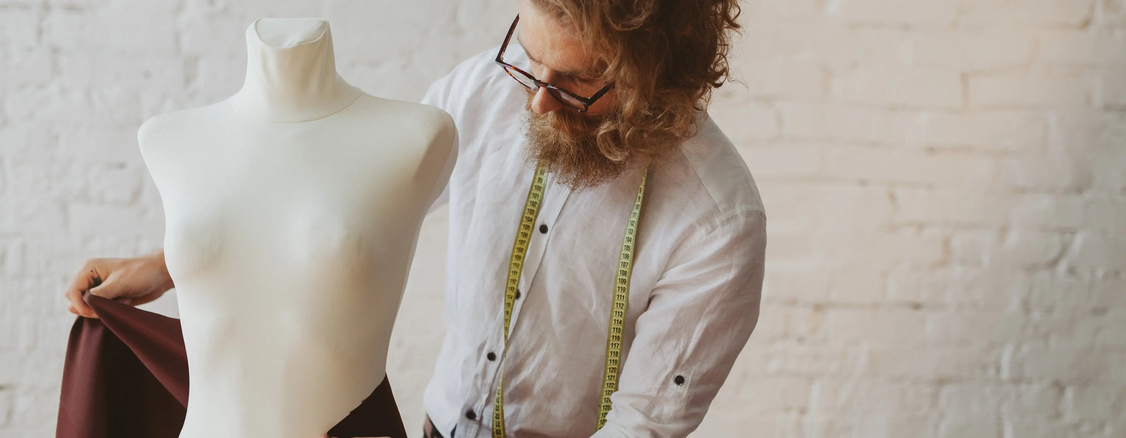 Foto de homem jovem fazendo experimentos com tecido em uma manequim de costura.