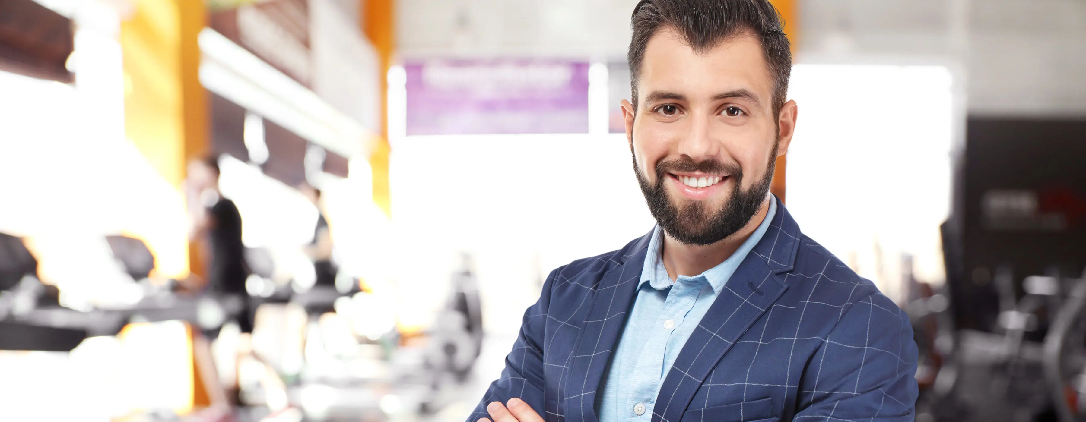 Foto em close de rosto de homem sorrindo, usando terno e camisa social, dentro de uma academia.