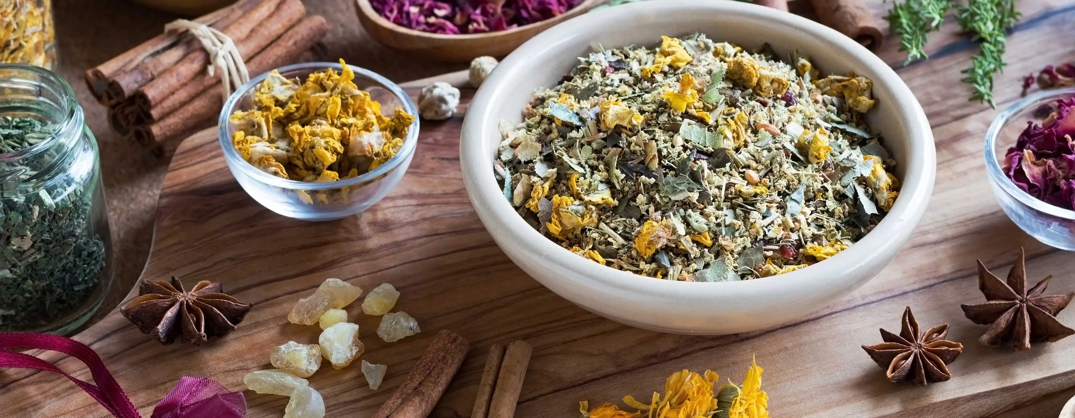 Foto em close de mesa com potes com plantas medicinais, ervas para chá, cristais e palitos de canela.