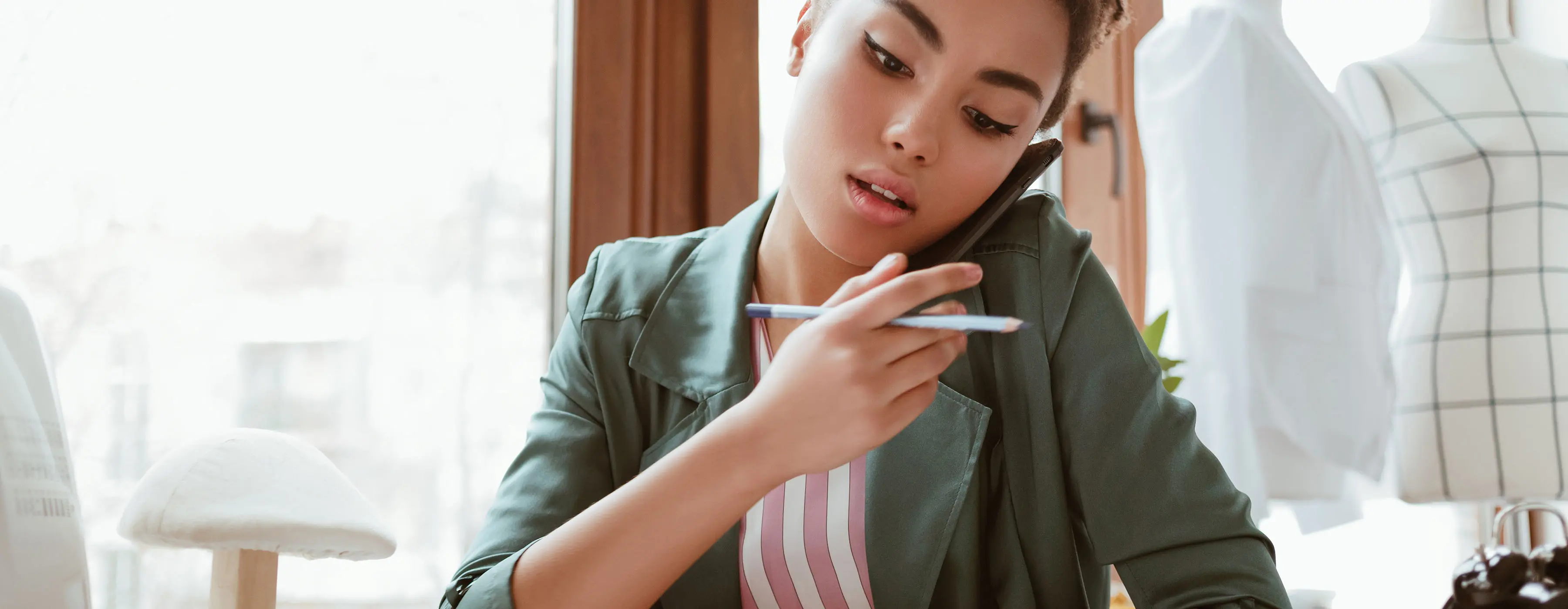Foto em close de uma moça, em um ateliê de moda, falando ao telefone.