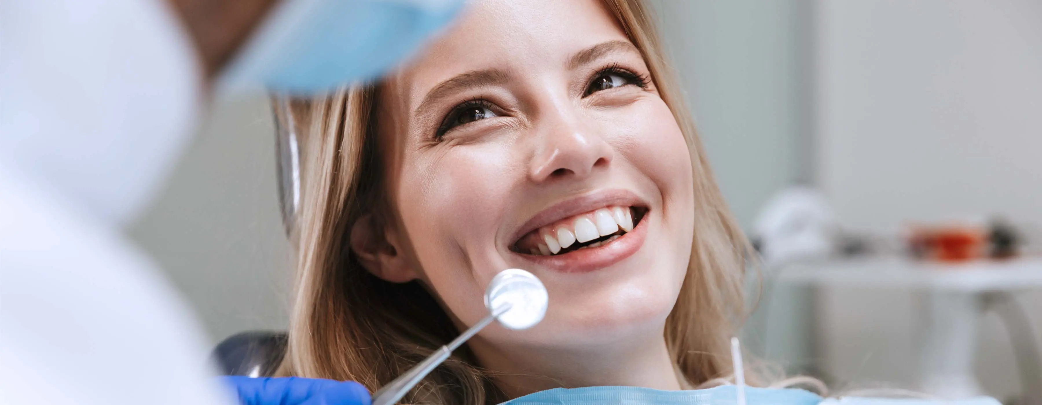 Foto em close de paciente sorrindo ao receber atendimento de dentista