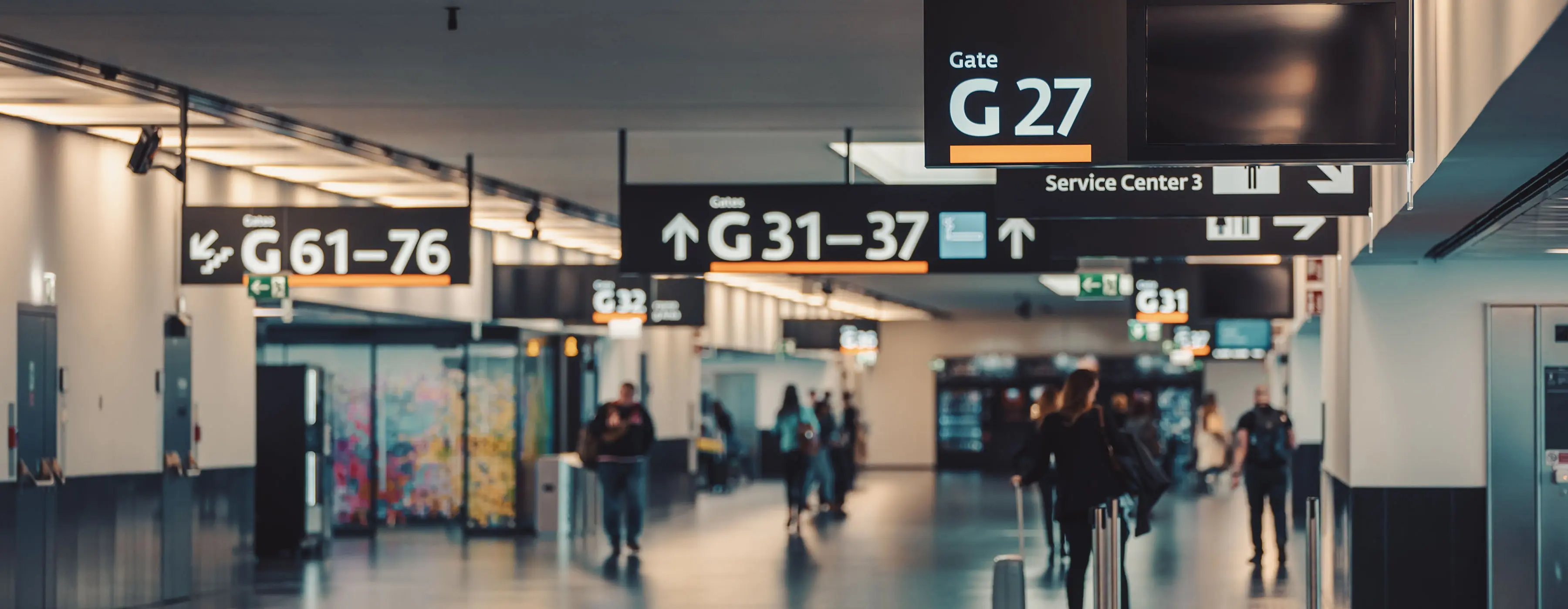 Foto de um corredor em um aeroporto, dando destaque aos layouts, informações e sinalizações das placas nos portões de embarque.