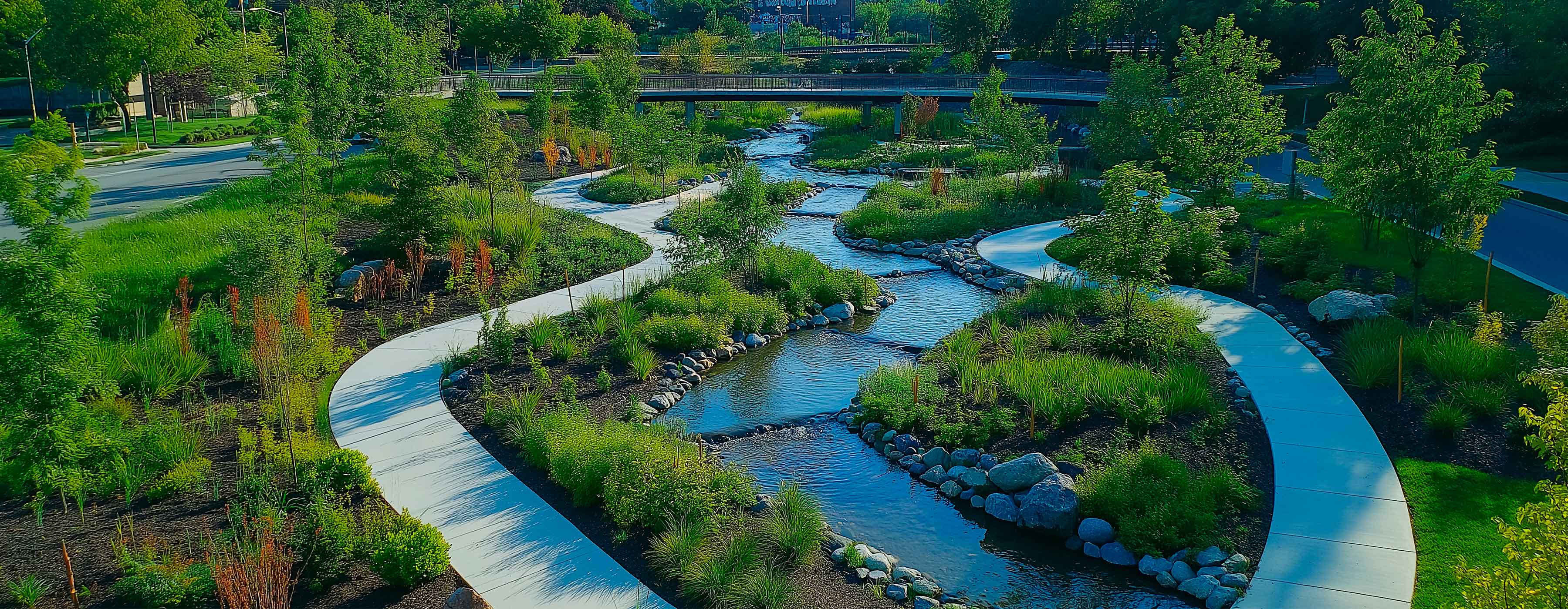 Foto de um espaço aberto com grama, árvores e um pequeno rio ao centro.