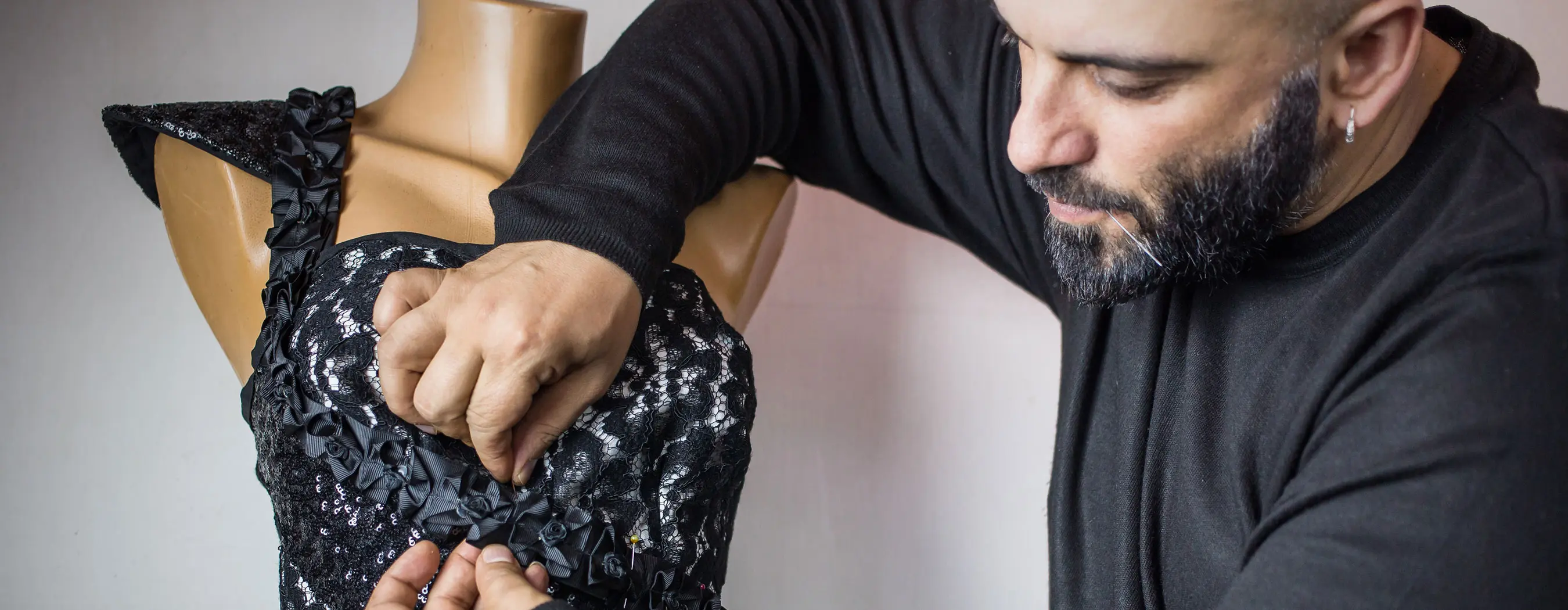 Foto de um homem fazendo costuras em um vestido pendurado em um manequim.