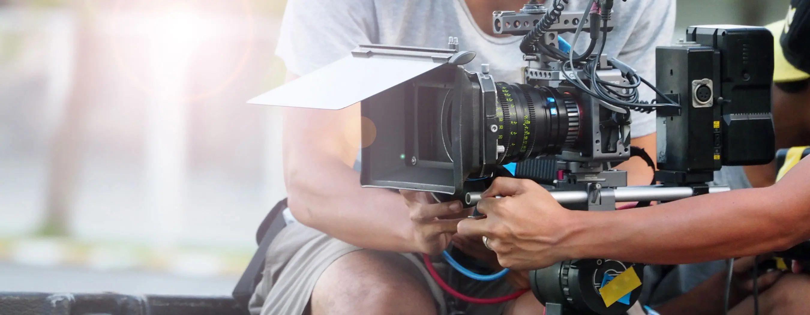 Foto em close de uma câmera de filmagem profissional manuseada por duas pessoas.