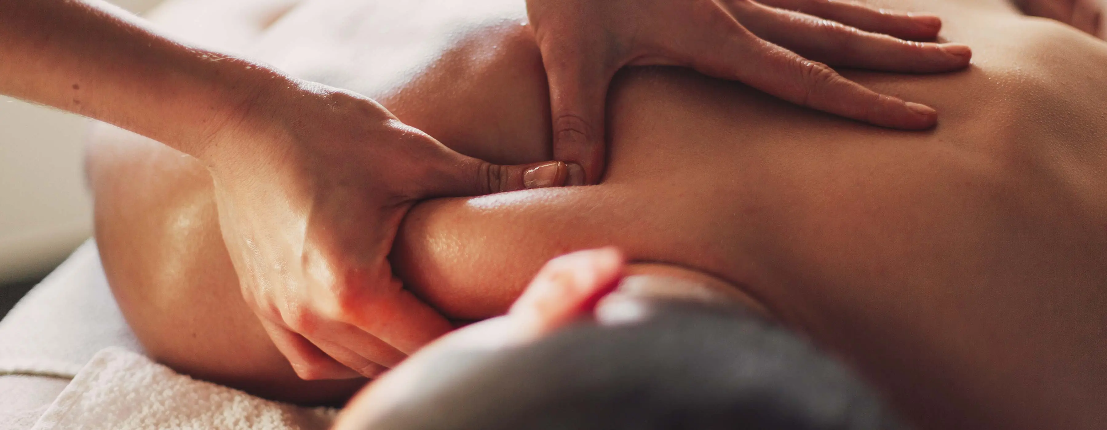 Foto em close das mãos de uma profissional de saúde aplicando massagem nas costas de um cliente deitado numa maca.