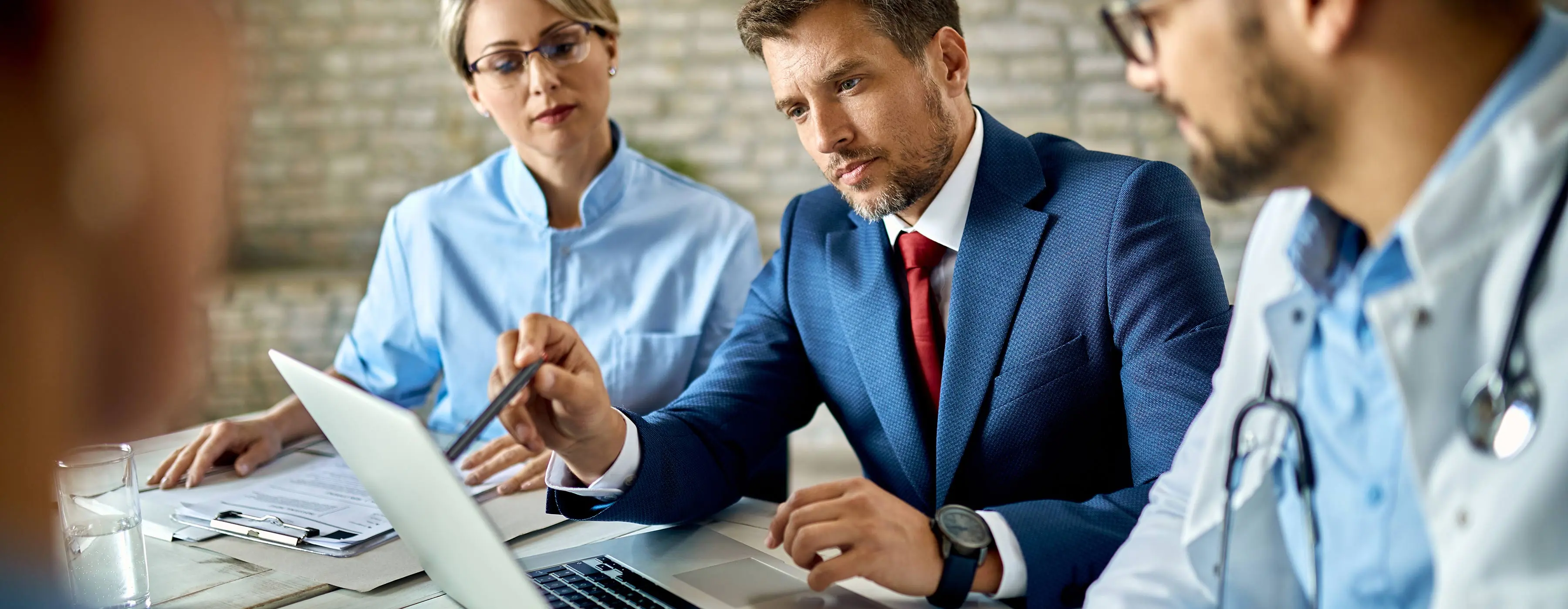 Foto de profissionais da saúde, durante reunião. Homem aponta para a tela do notebook e as demais pessoas prestam atenção.