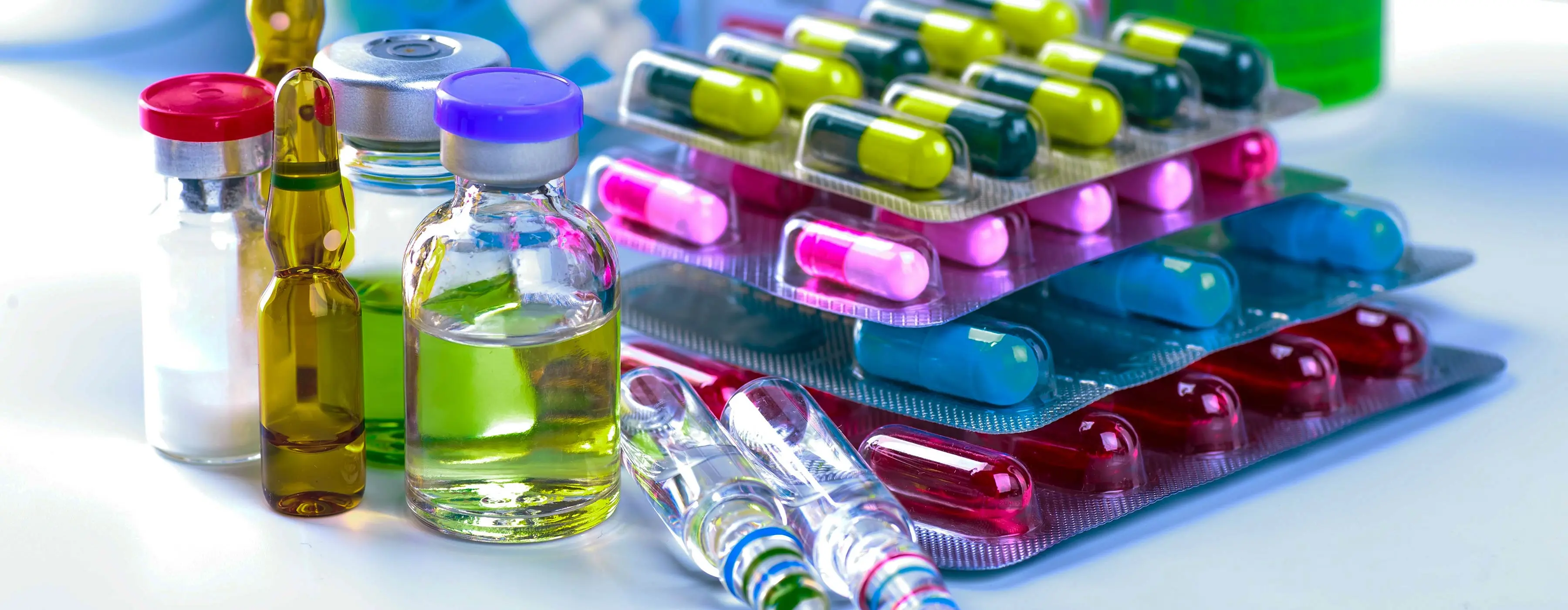 Foto em close de ampolas de medicamentos. Ao lado das ampolas, várias cartelas de medicamentos empilhadas.
