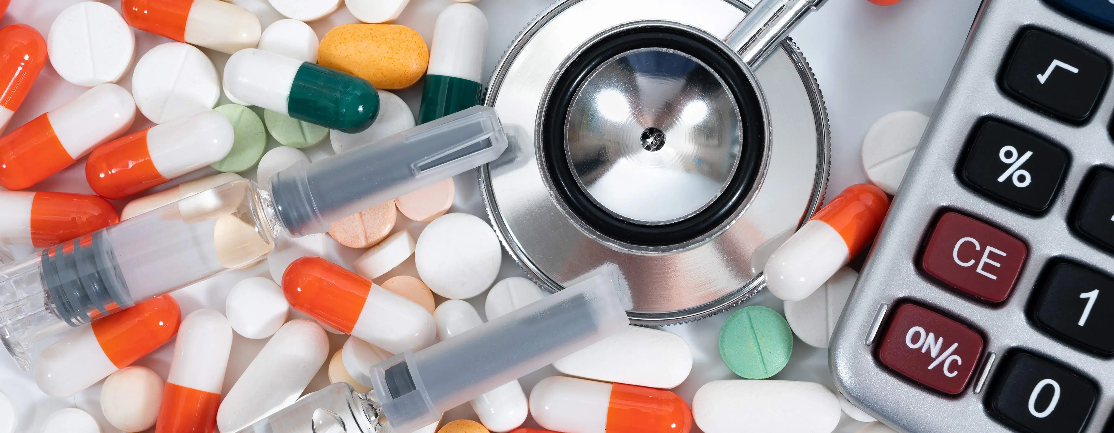 Foto em close de pílulas de diferentes tamanhos e cores, de ampolas de medicação, de calculadora e de um medidor de medicamentos.