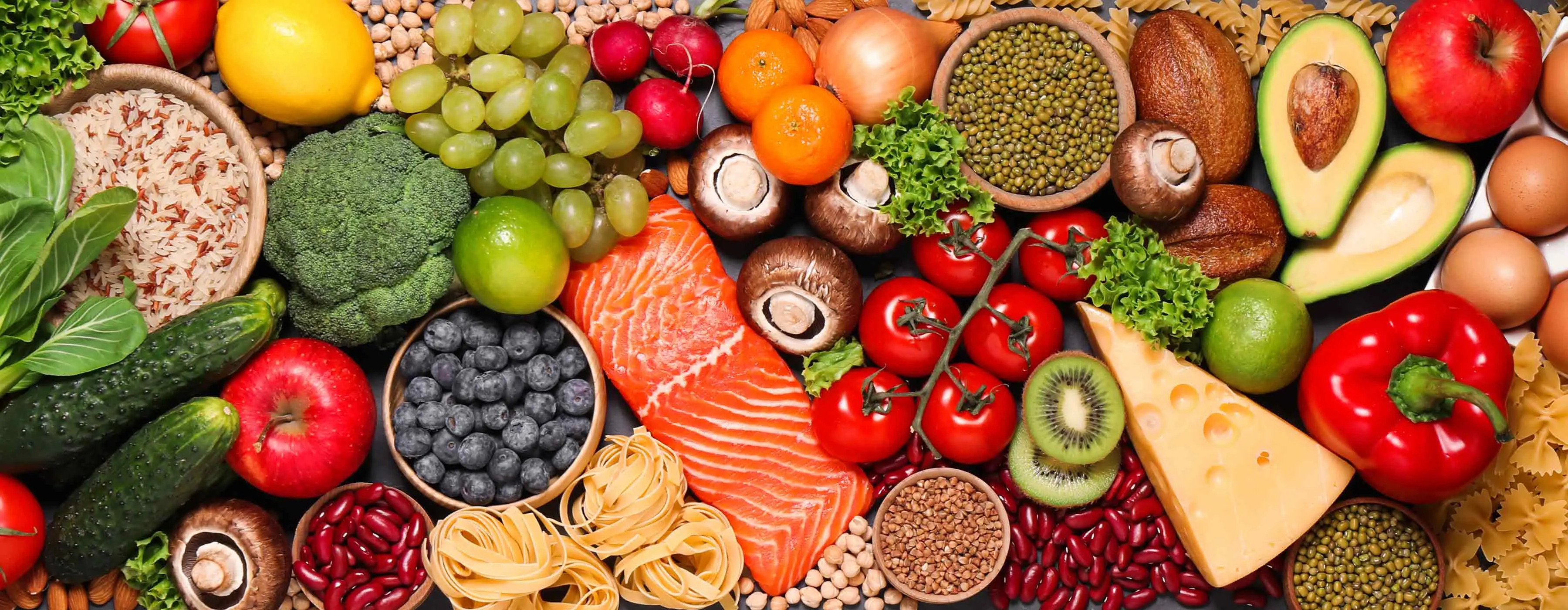 Foto em close de vários legumes, frutas, grãos de diferentes tipos e formatos dispostos em uma superfície plana