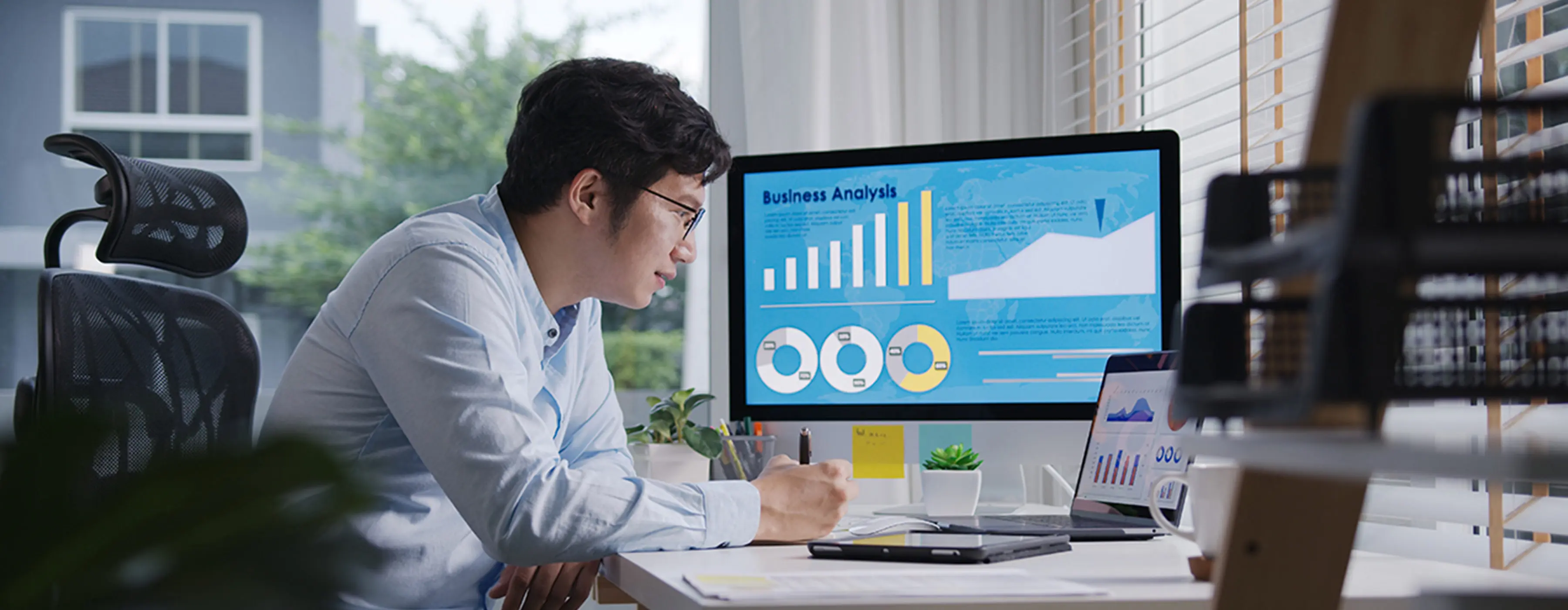 Foto de homem observando dados em monitor de computador e notebook em Business Analysis em sala de escritório.