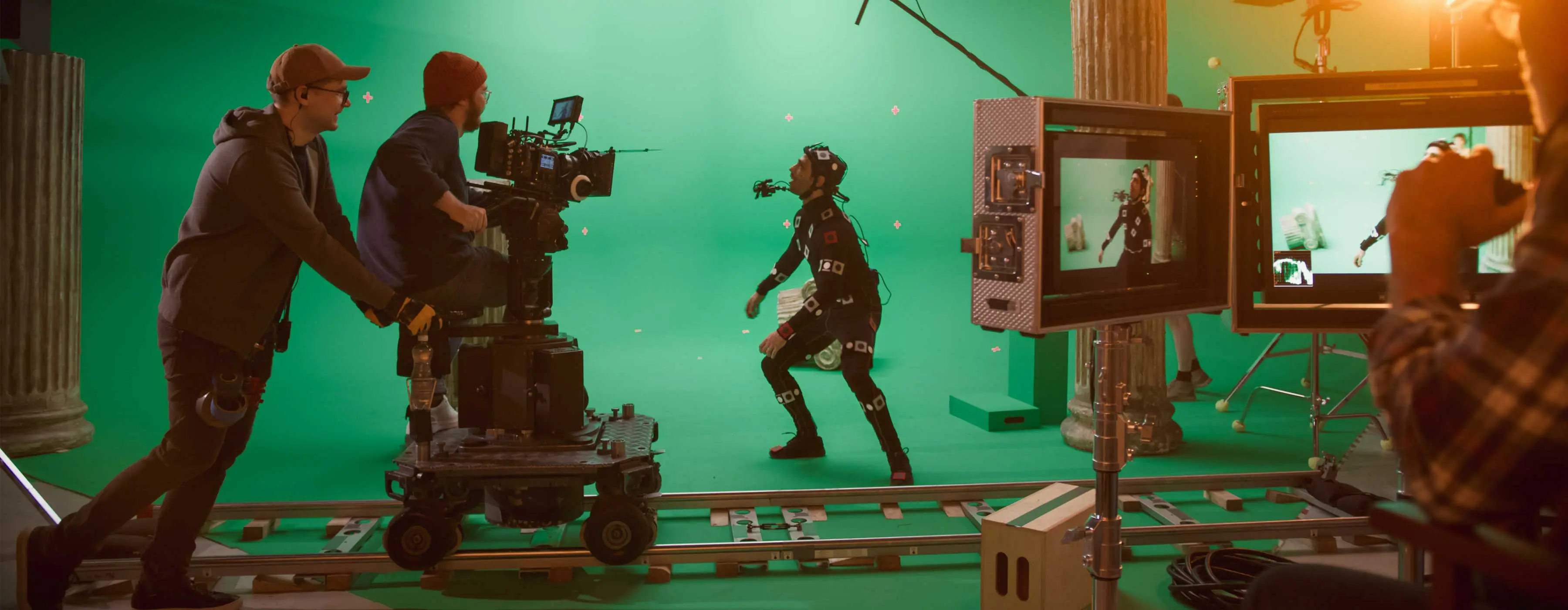 Foto de uma pessoa com macacão com câmera acoplada em estúdio de gravação e equipe de set com filmadoras profissionais.