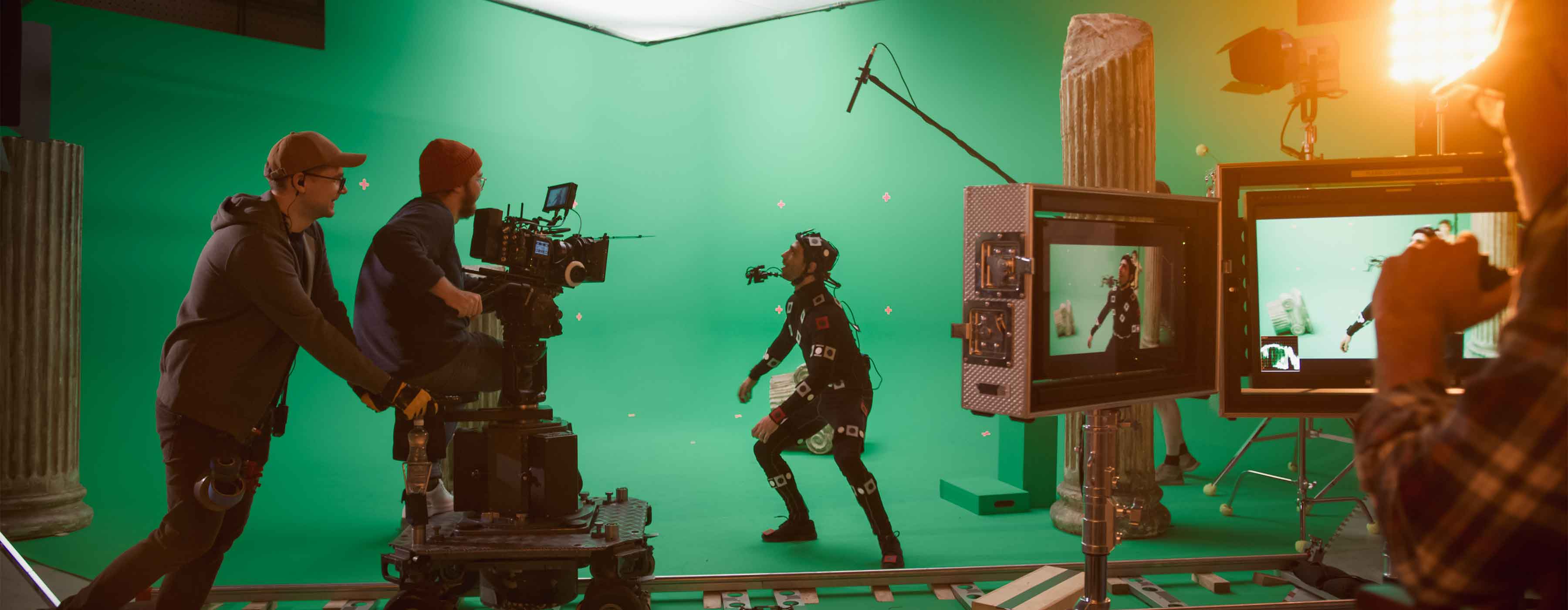 Estúdio de gravação com fundo verde, câmera de filmagem e pessoa usando traje de captura de movimento.