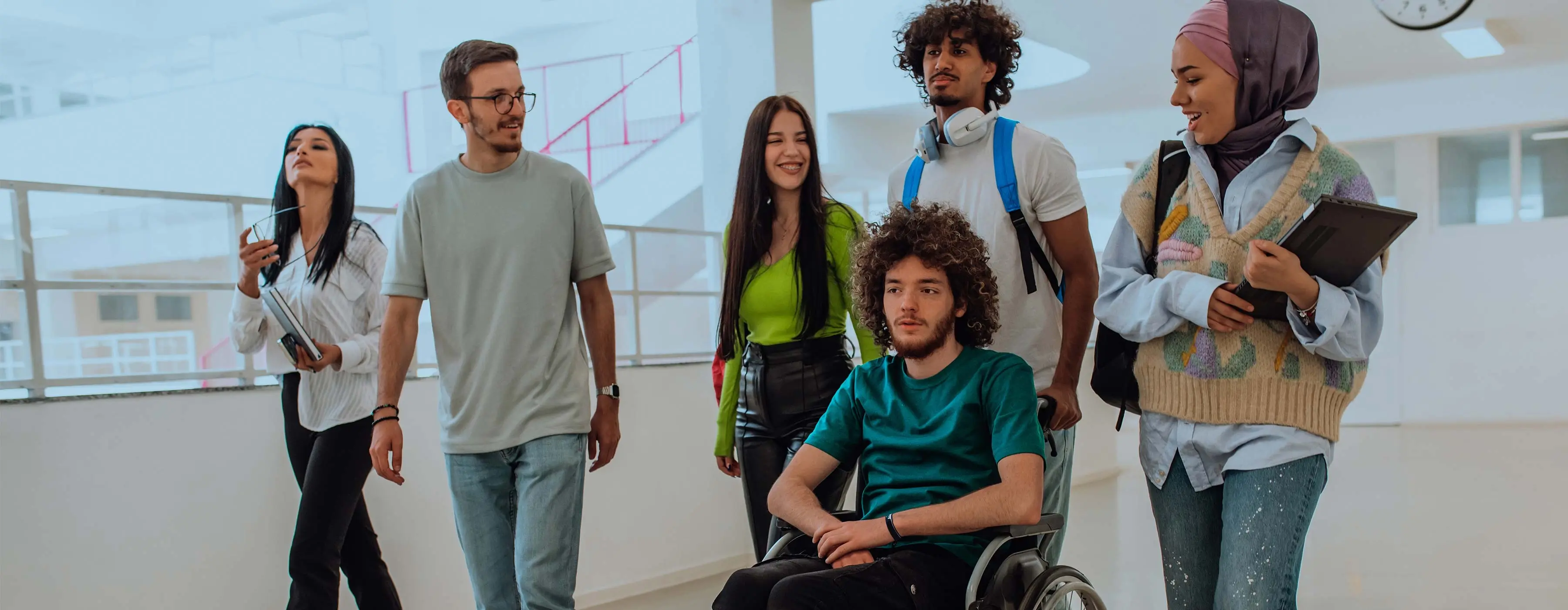 Foto de um grupo de pessoas diversas em suas etnias, religiões e deficiência física conversando em um corredor.
