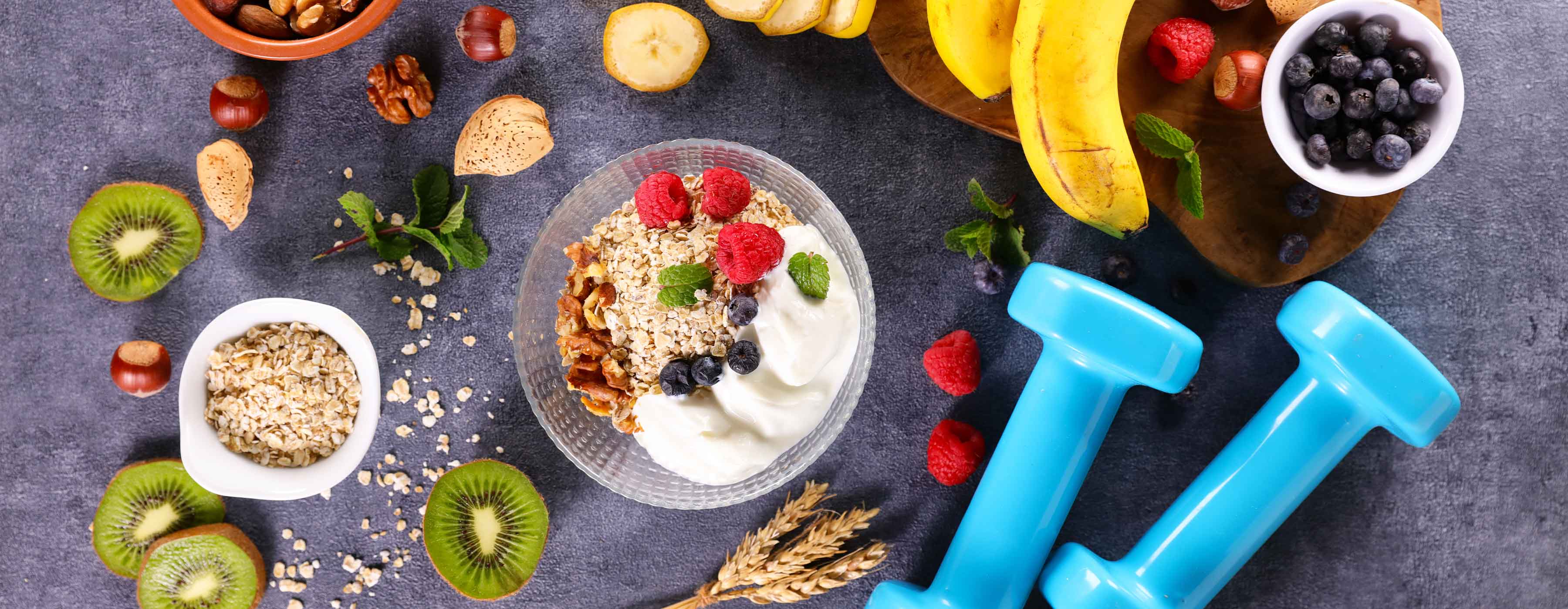 Pós-graduação em Nutrição e Exercício: saúde, comportamento e performance - foto de uma mesa com uma pequena tijela de vidro com iogurte, aveia, frutas, algumas oleaginosas e dois halteres.
