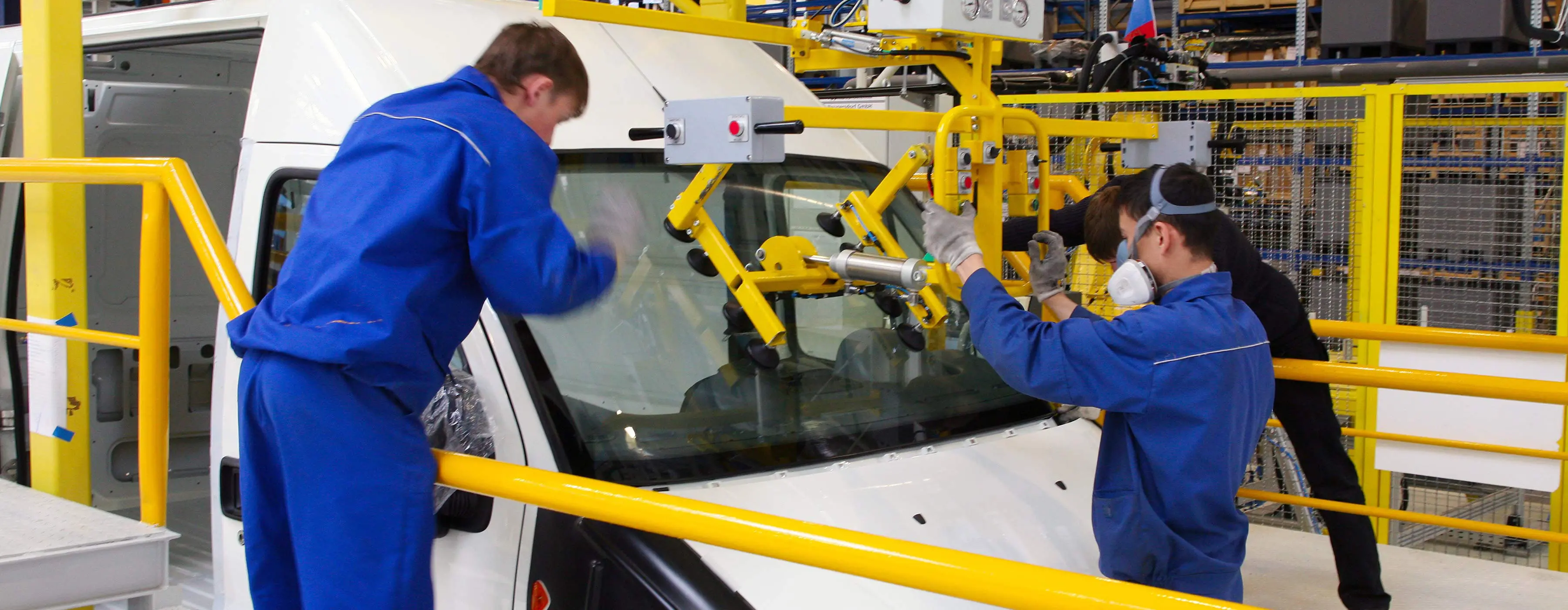 Foto de duas pessoas manuseando máquinas para fixar vidro em combi em indústria.