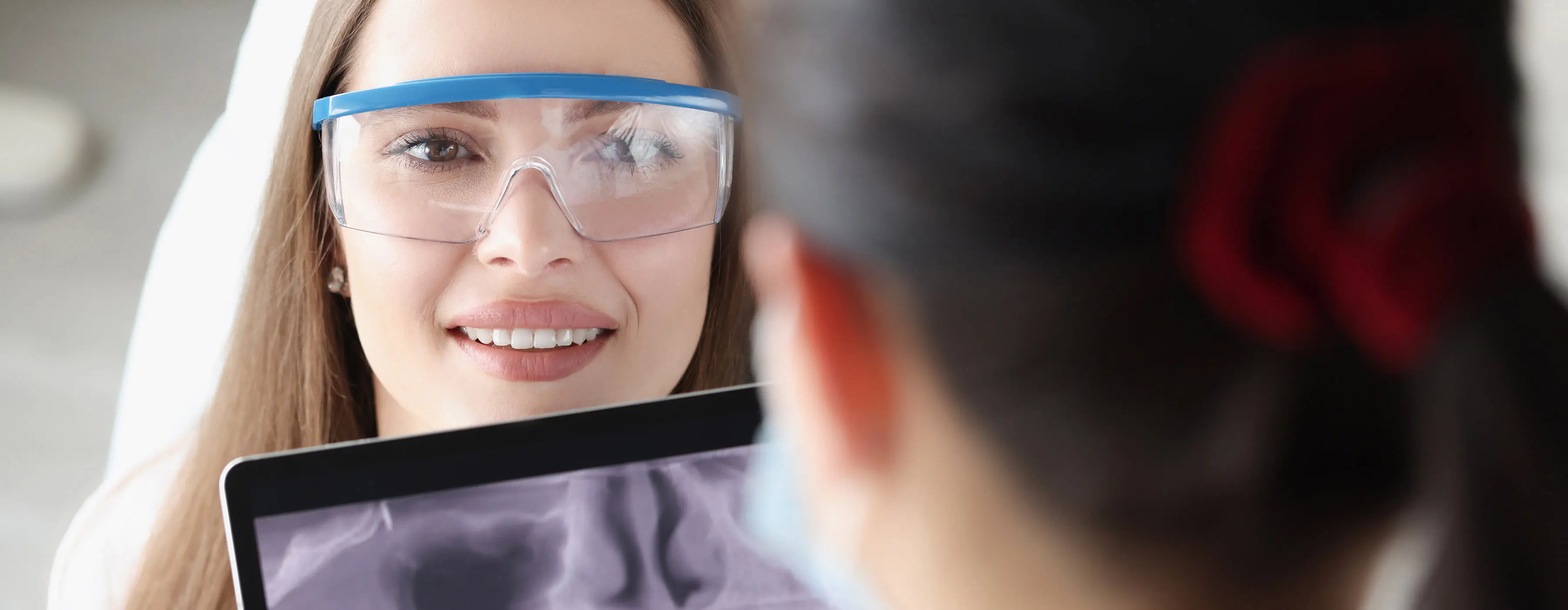 Foto de mulher com óculos de proteção mostrando imagem de radiologia digital odontológica para paciente.