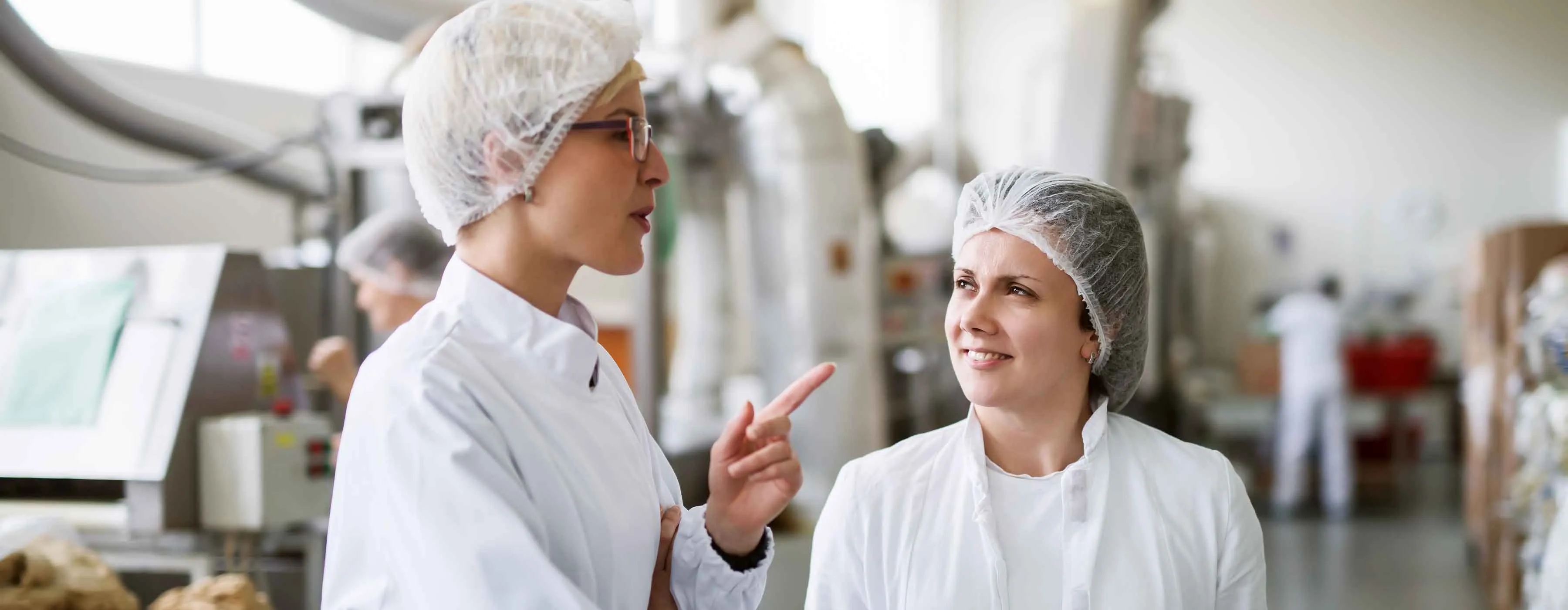 Duas profissionais da nutrição conversam em cozinha industrial.