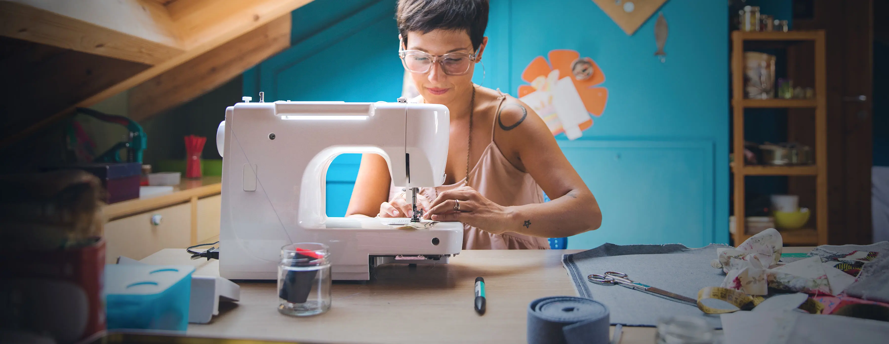 Foto de uma mulher com óculos manuseando tecido em uma máquina de costura.