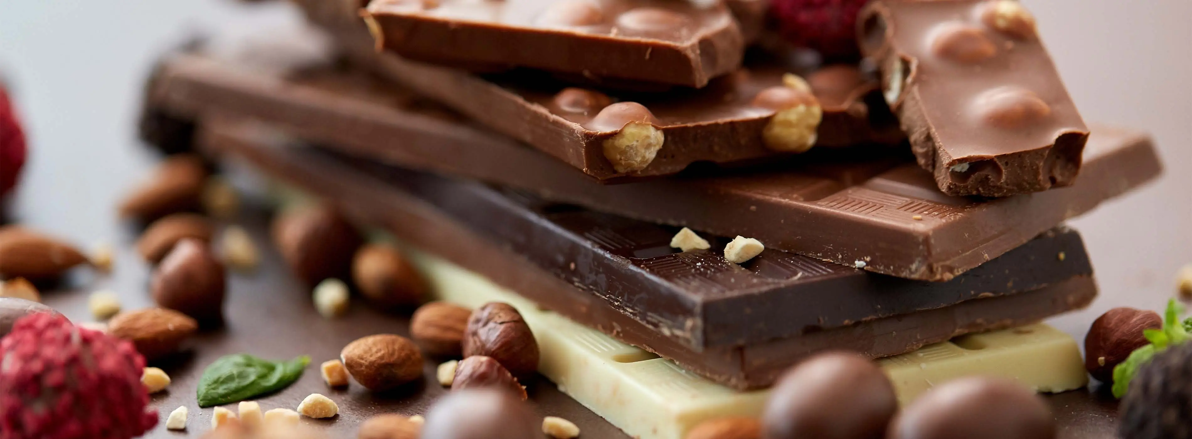 Foto em close de várias barras de chocolate empilhadas, com sementes e outros ingredientes dispostos ao redor.