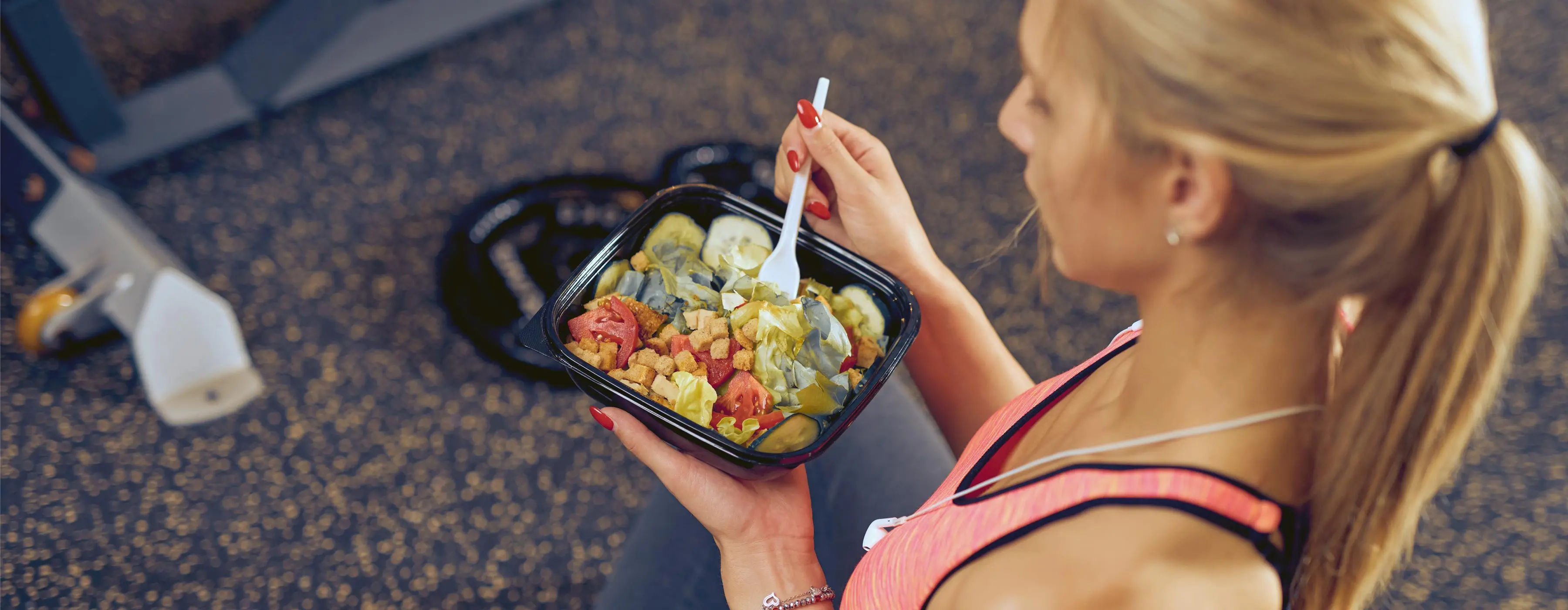 Foto de uma mulher comendo marmita de salada e legumes em academia de ginástica.