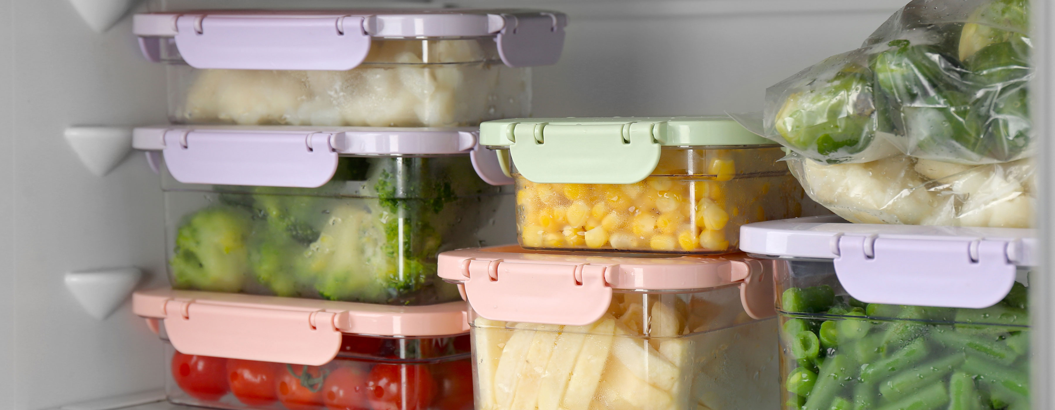 Técnicas de Congelamento - foto de seis potes  com tampas coloridas e  um saco plástico com  vegetais guardados dentro  de uma prateleira de geladeira.