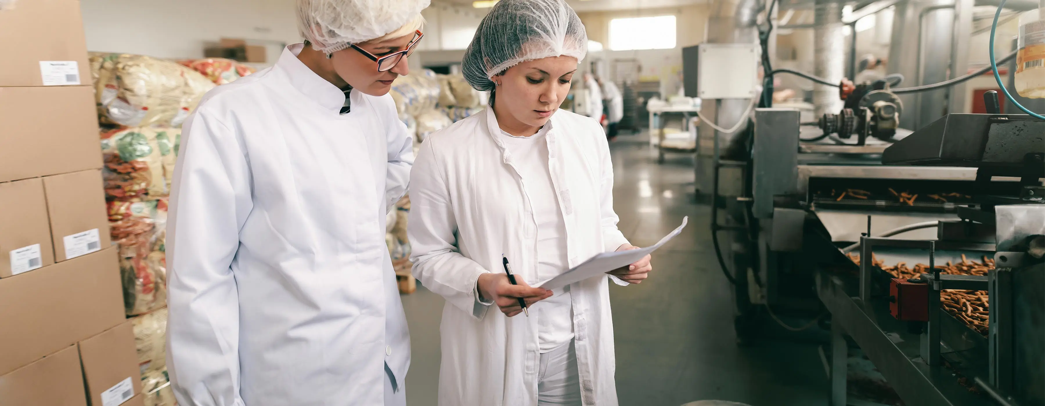 Foto de duas mulheres, em uma indústria de alimentação, realizando conferência de boas práticas de segurança de alimentos.