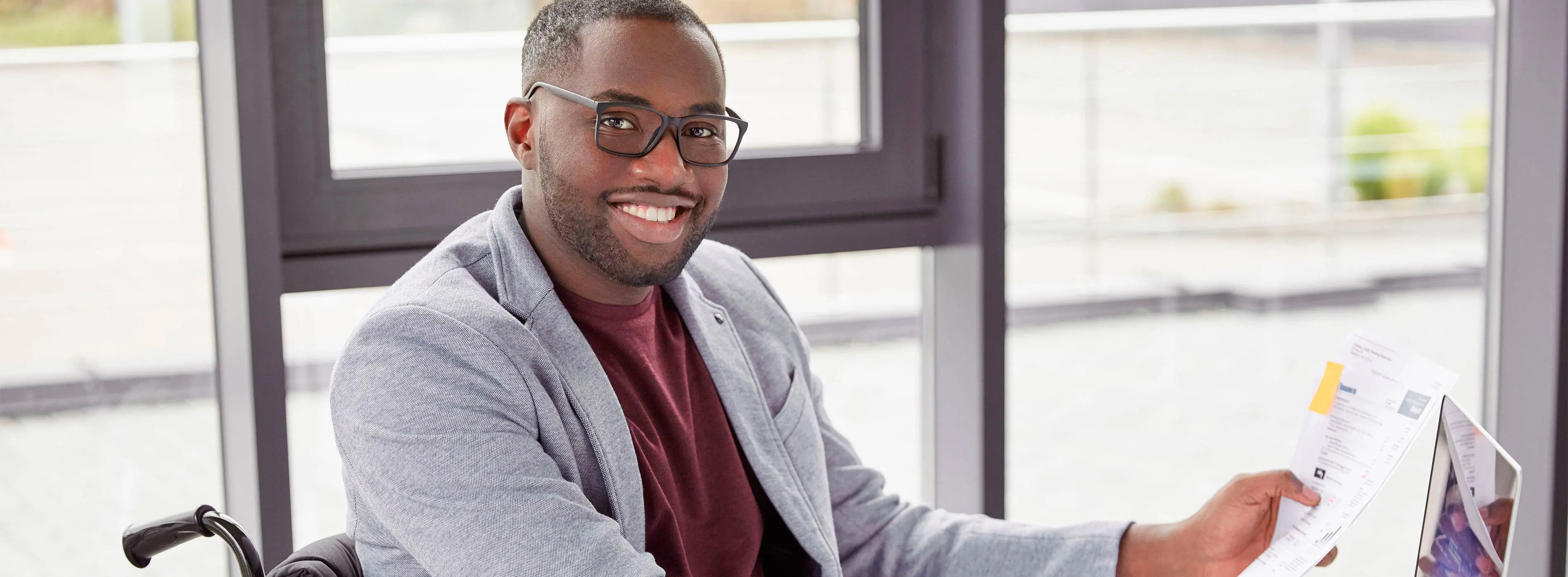 Foto de homem negro cadeirante segurando papeis e sorrindo para a foto.