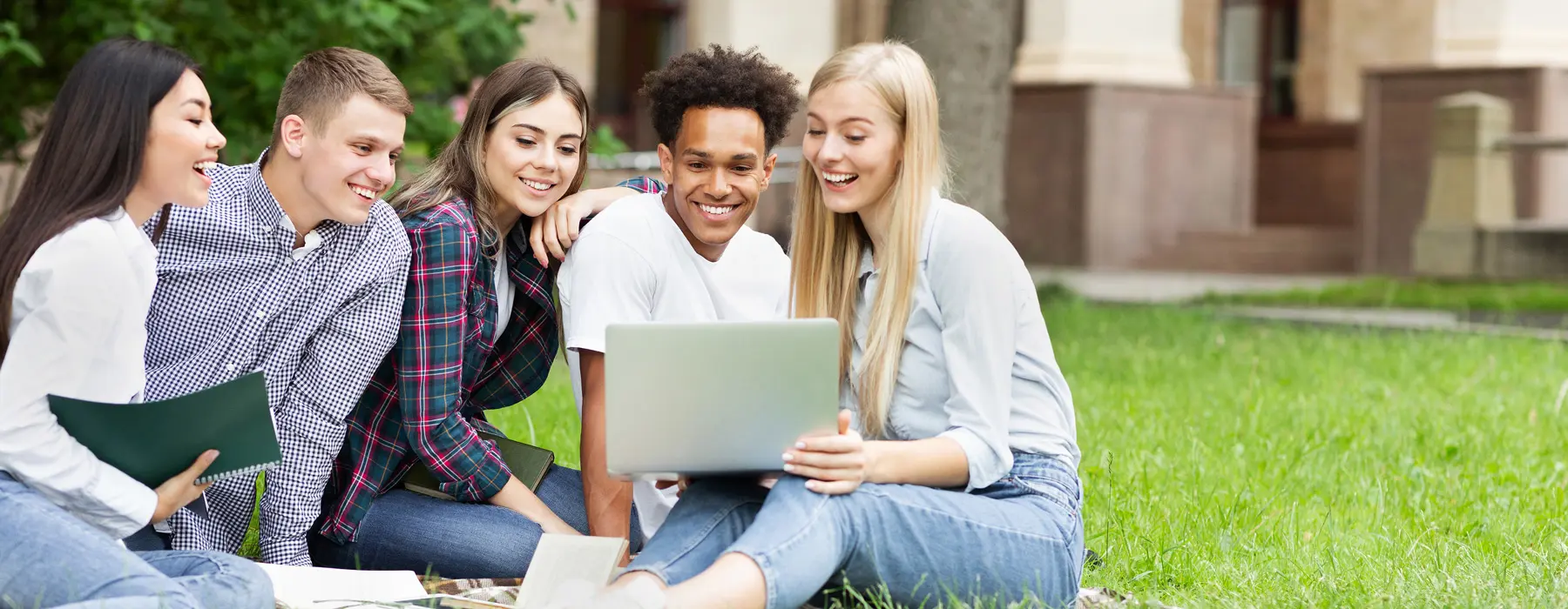 Foto de grupo de jovens sentados na grama olhando um notebook