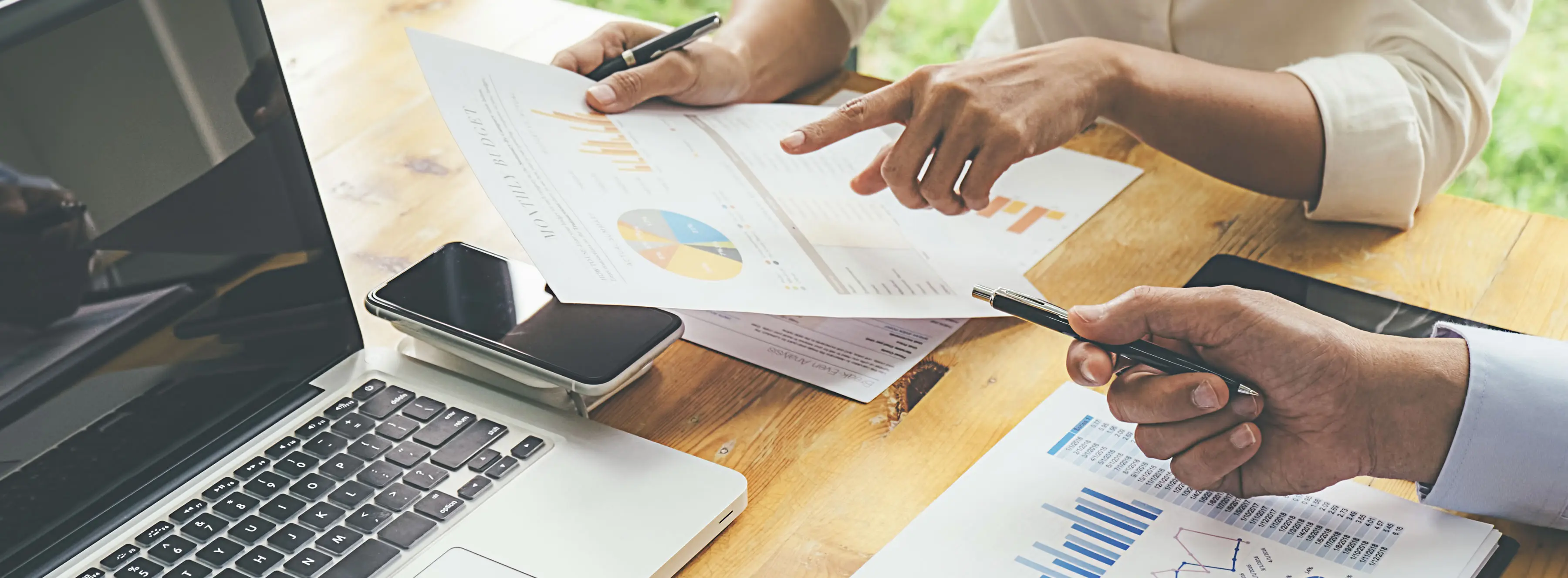 Foto de duas mãos sobre uma mesa analisando relatórios e gráficos.