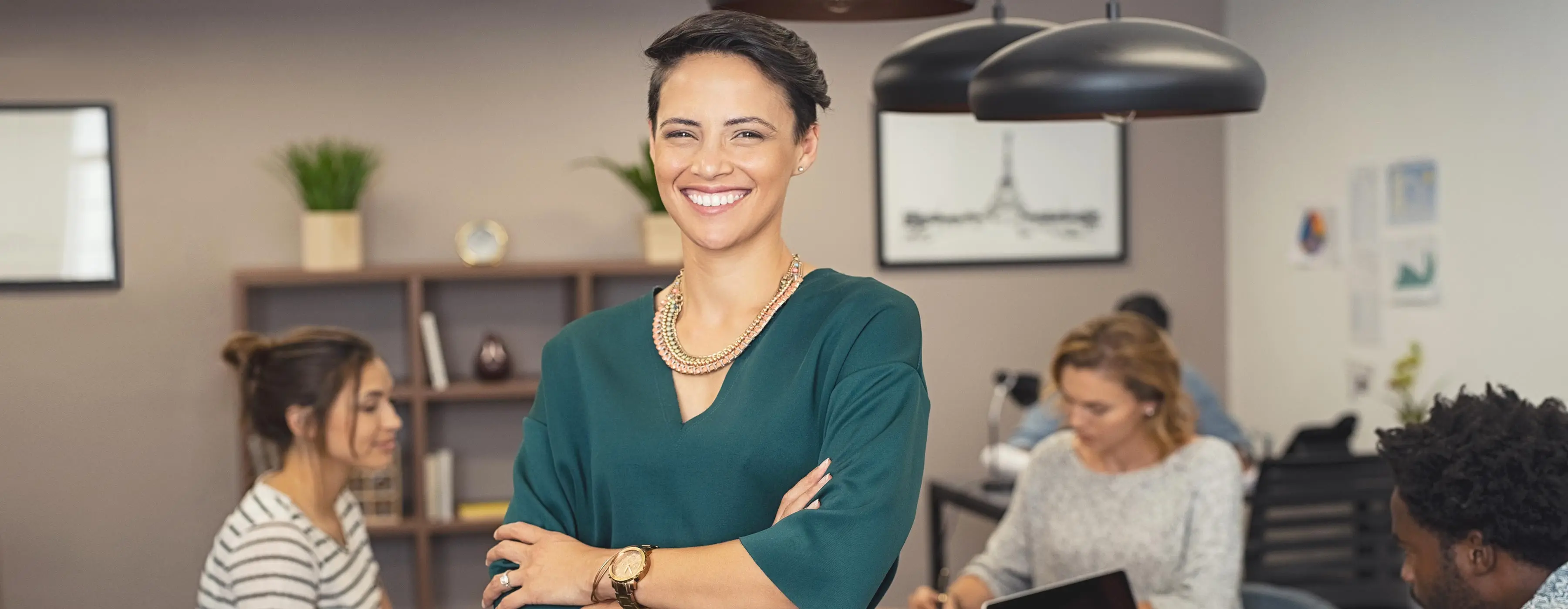 Foto de mulher sorridente com os braços cruzados em sala com outras mulheres ao fundo