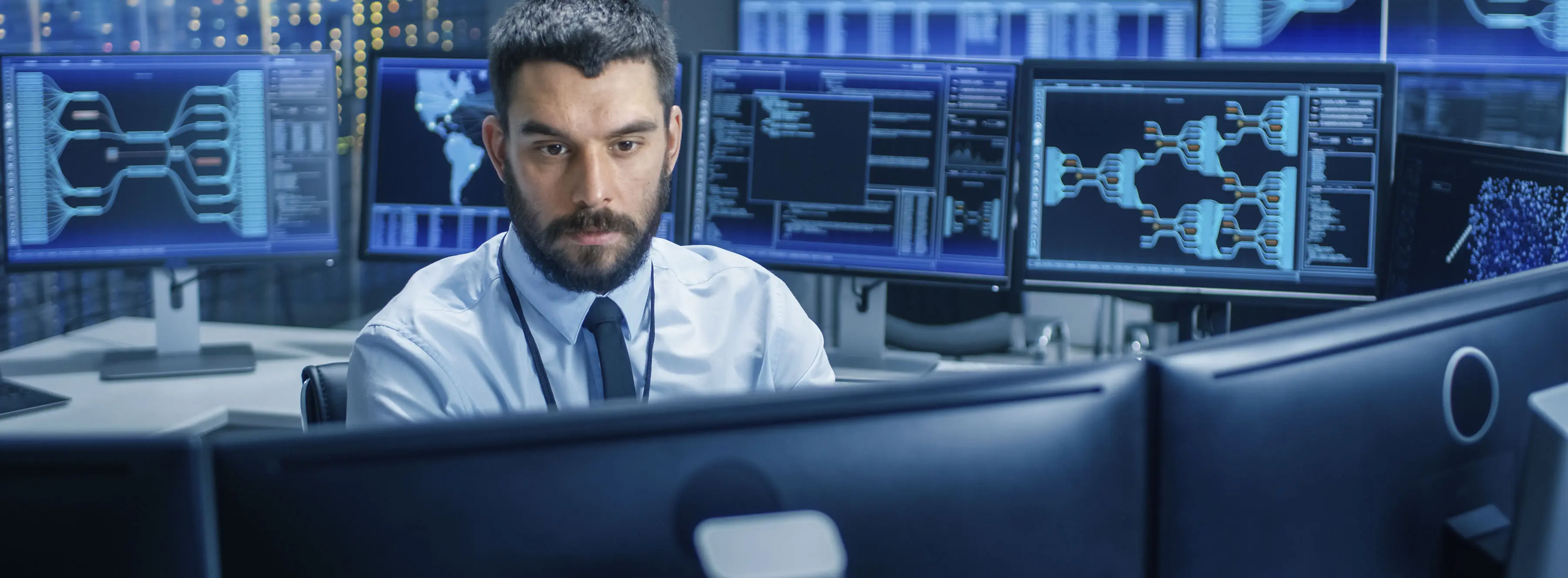 Foto de homem em uma sala repleta de monitores ligados, observando com atenção um deles.