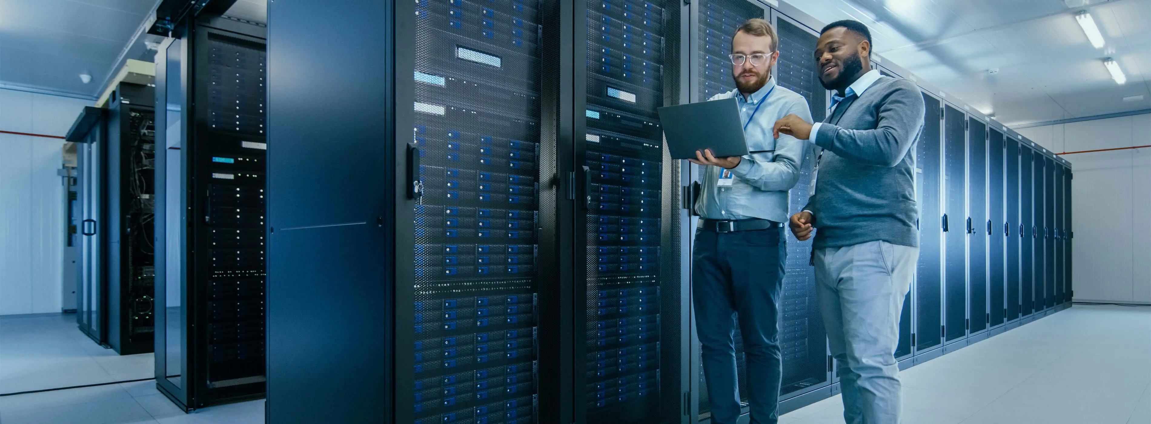 Foto de dois homens checando no mesmo notebook em data center de empresa.