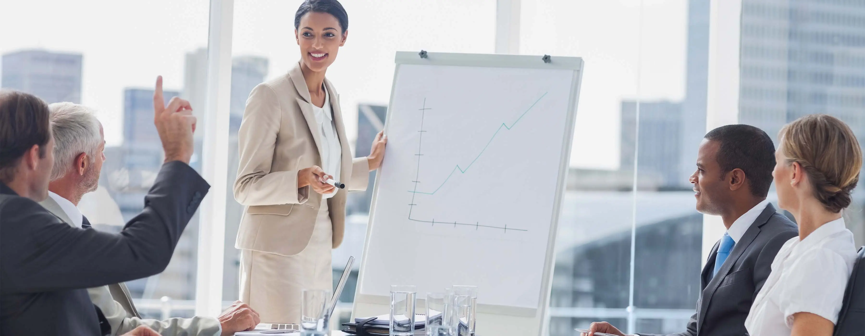 Foto de mulher apresentando gráfico em flip chart para grupo de pessoas em sala de reuniões de empresa.