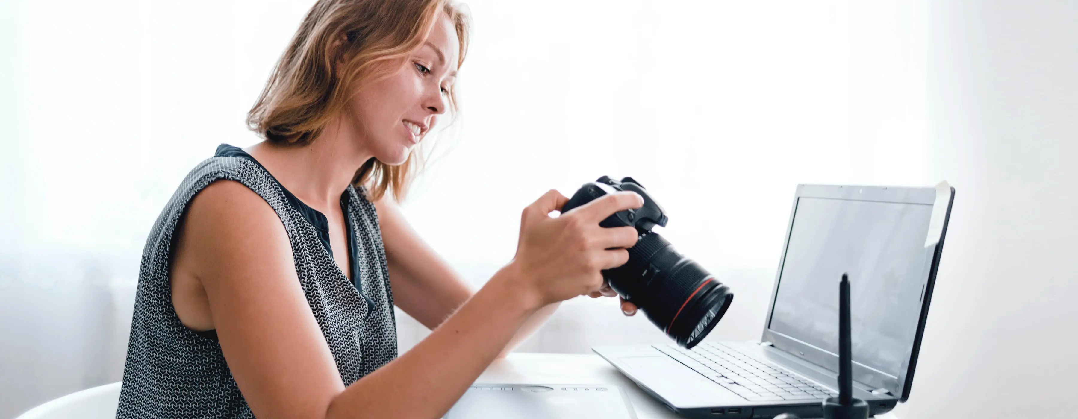 Foto de uma mulher jovem sorrindo, usando roupas formais, falando no celular e em um escritório.