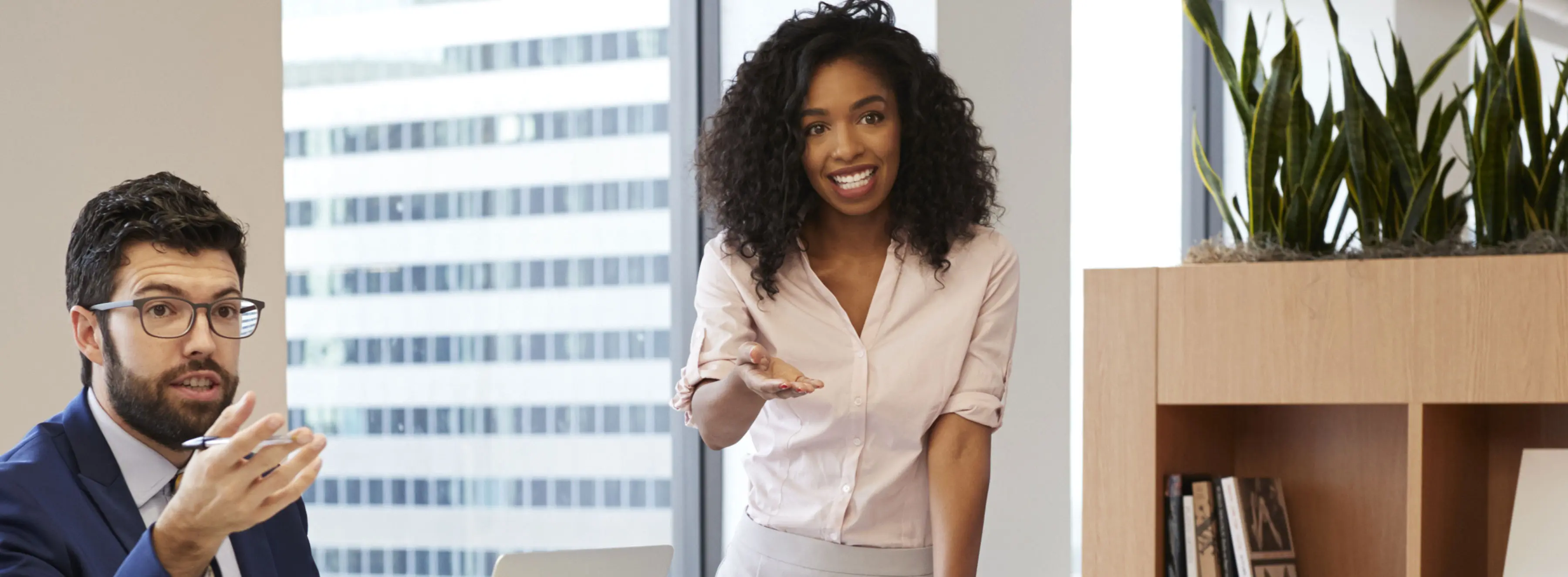Foto de uma mulher jovem sorridente, em ambiente corporativo, falando com colegas.