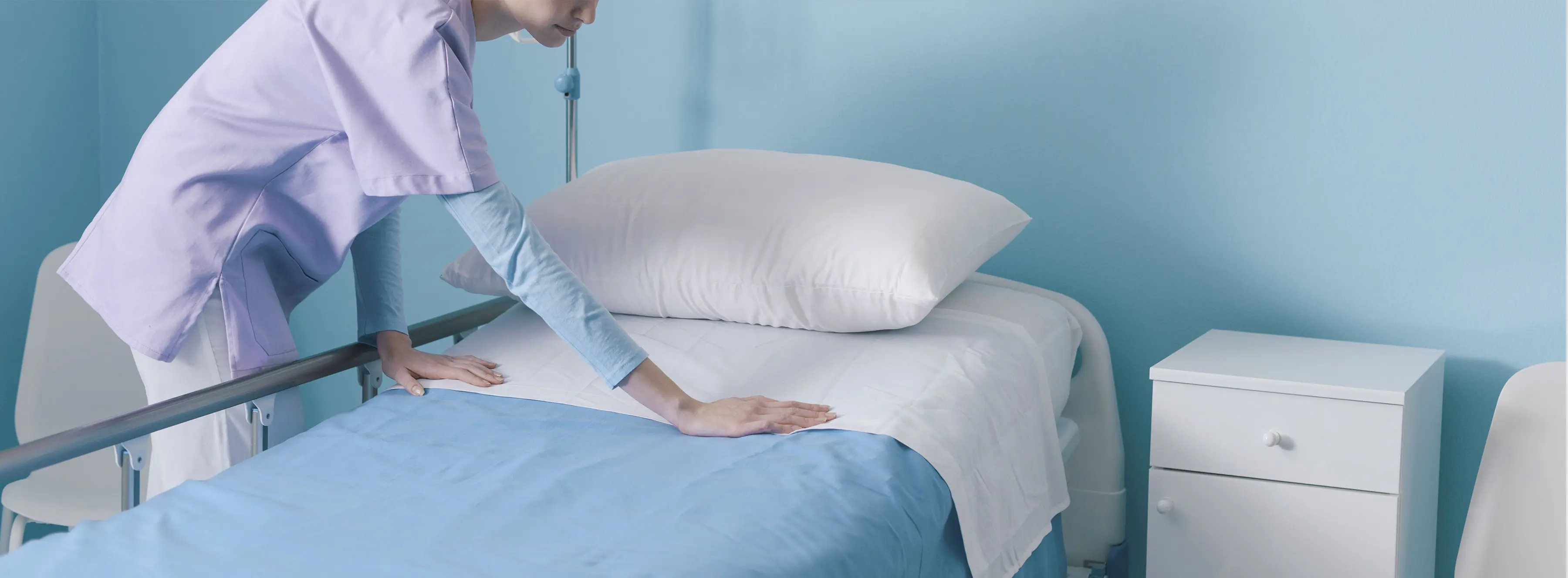 Foto de uma pessoa com uniforme de hospital arrumando uma cama.